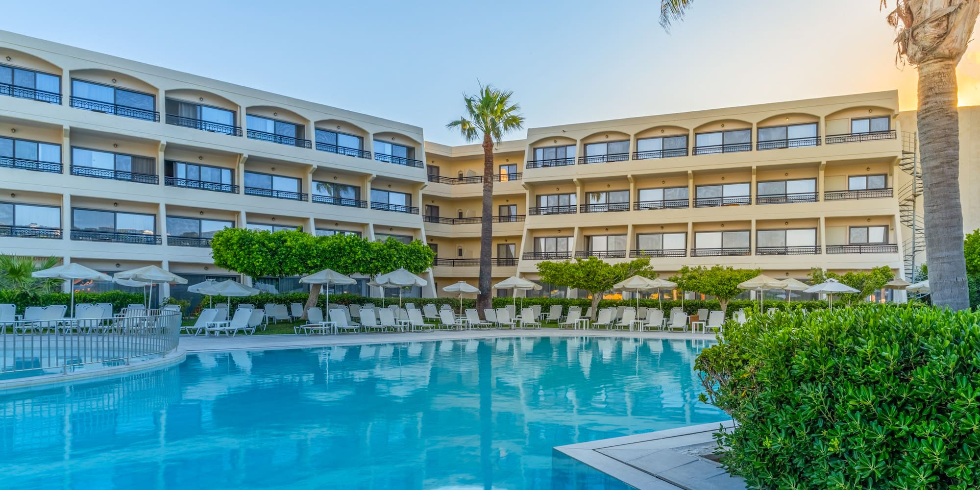 Resort hotel with blue swimming pool, palm trees, and sun loungers.