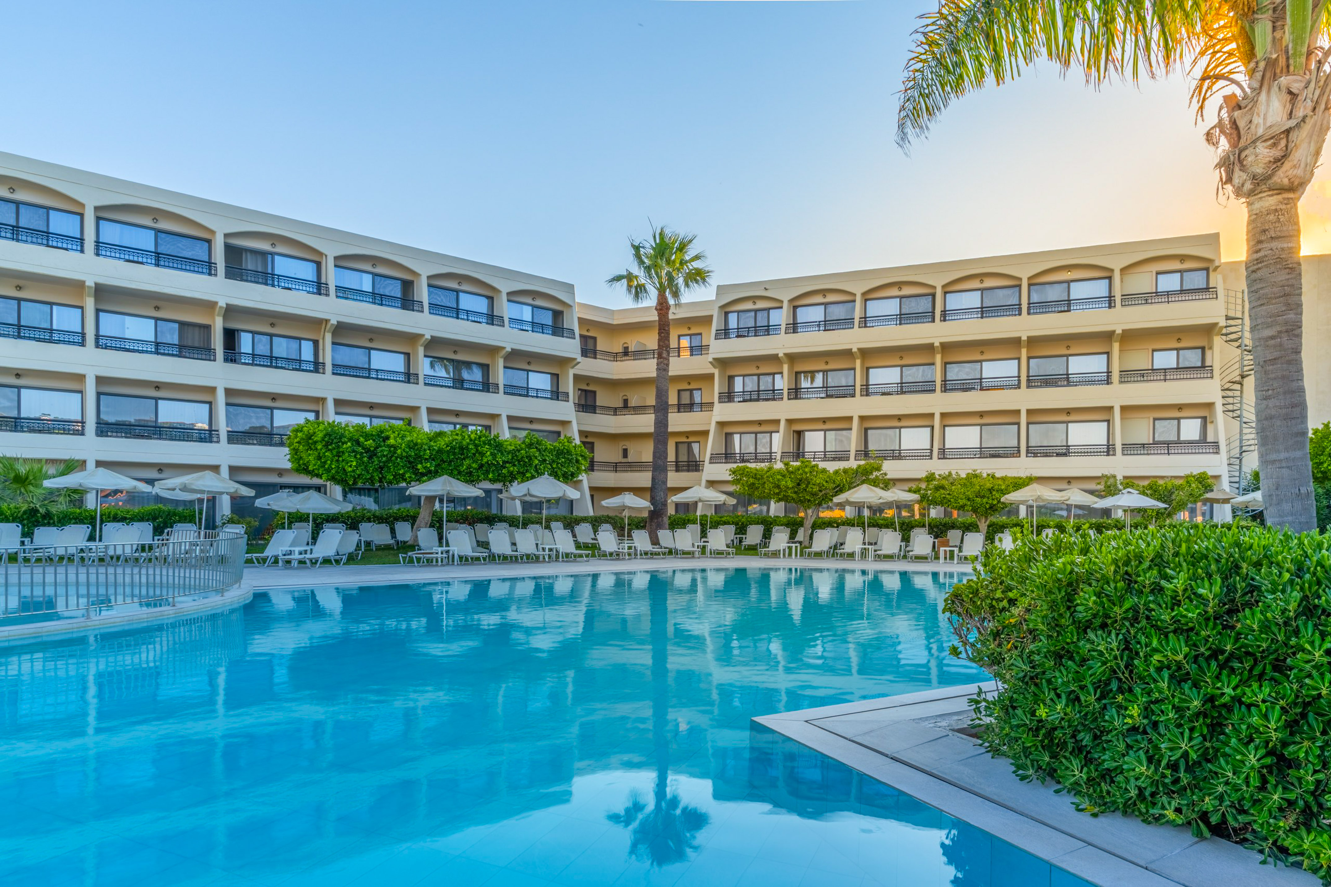 Resort hotel with blue swimming pool, palm trees, and sun loungers.