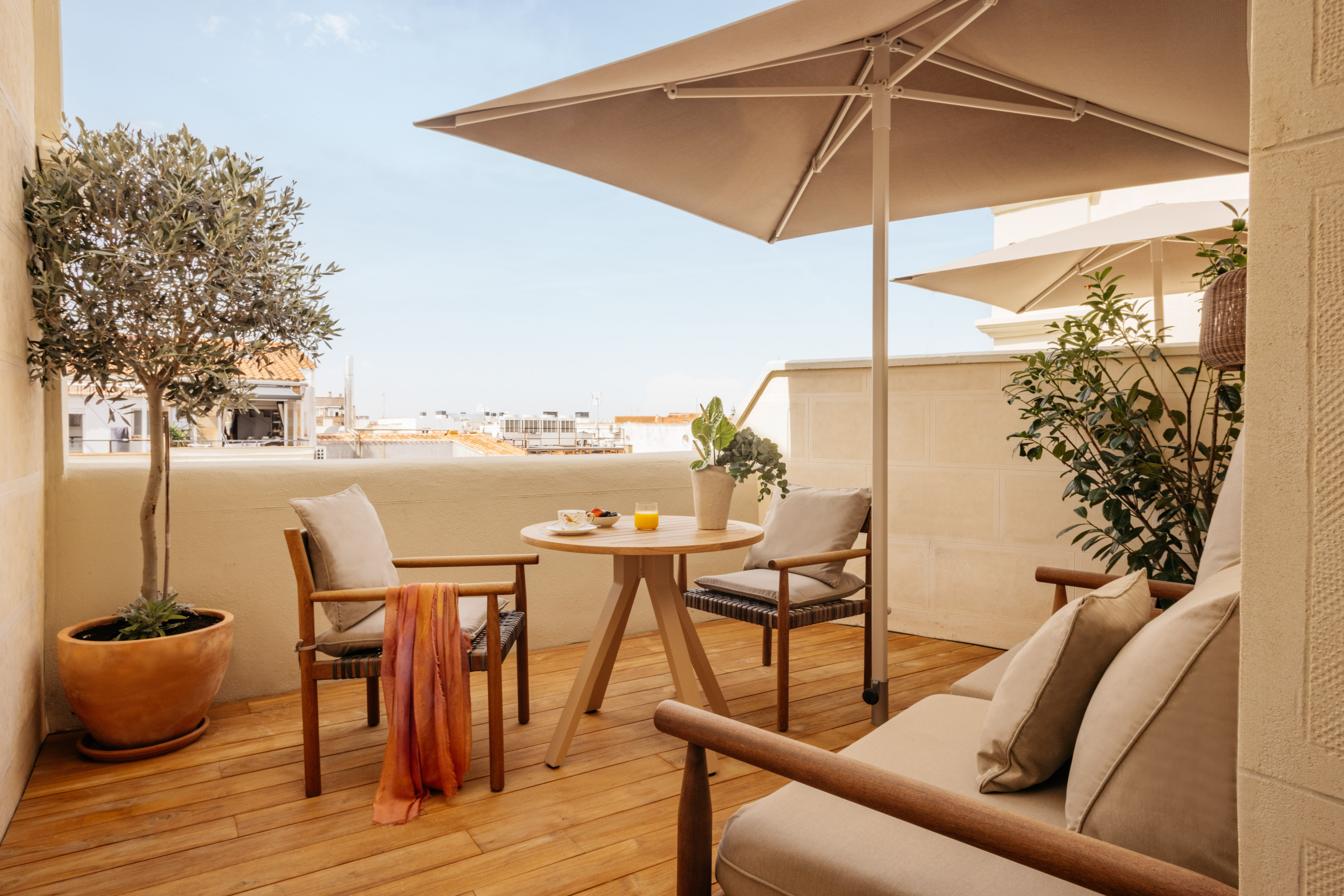 Wooden terrace with outdoor dining, lounge seating, olive tree, and umbrella.