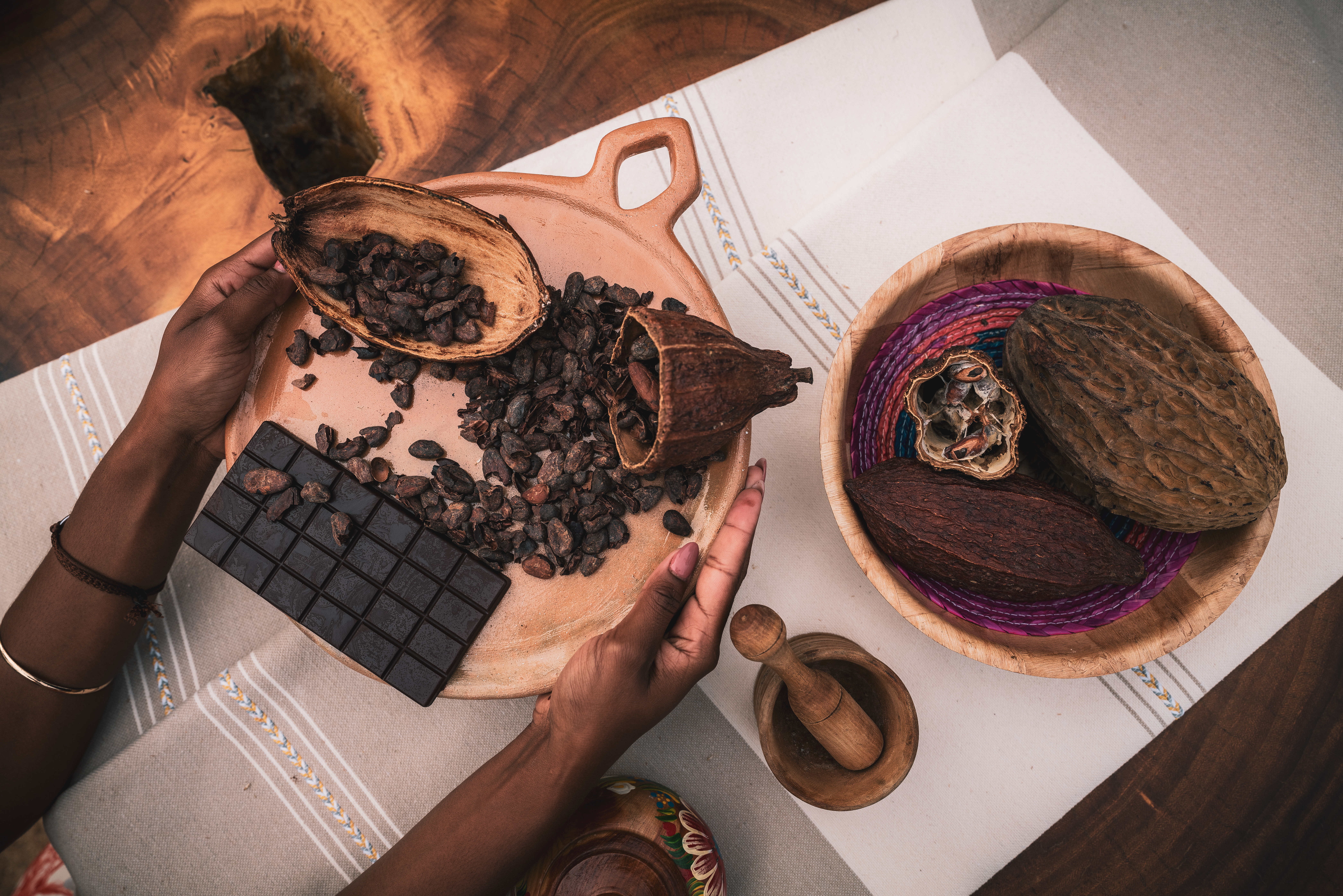 Cacao beans, chocolate bar, and pods with mortar and pestle on a table.