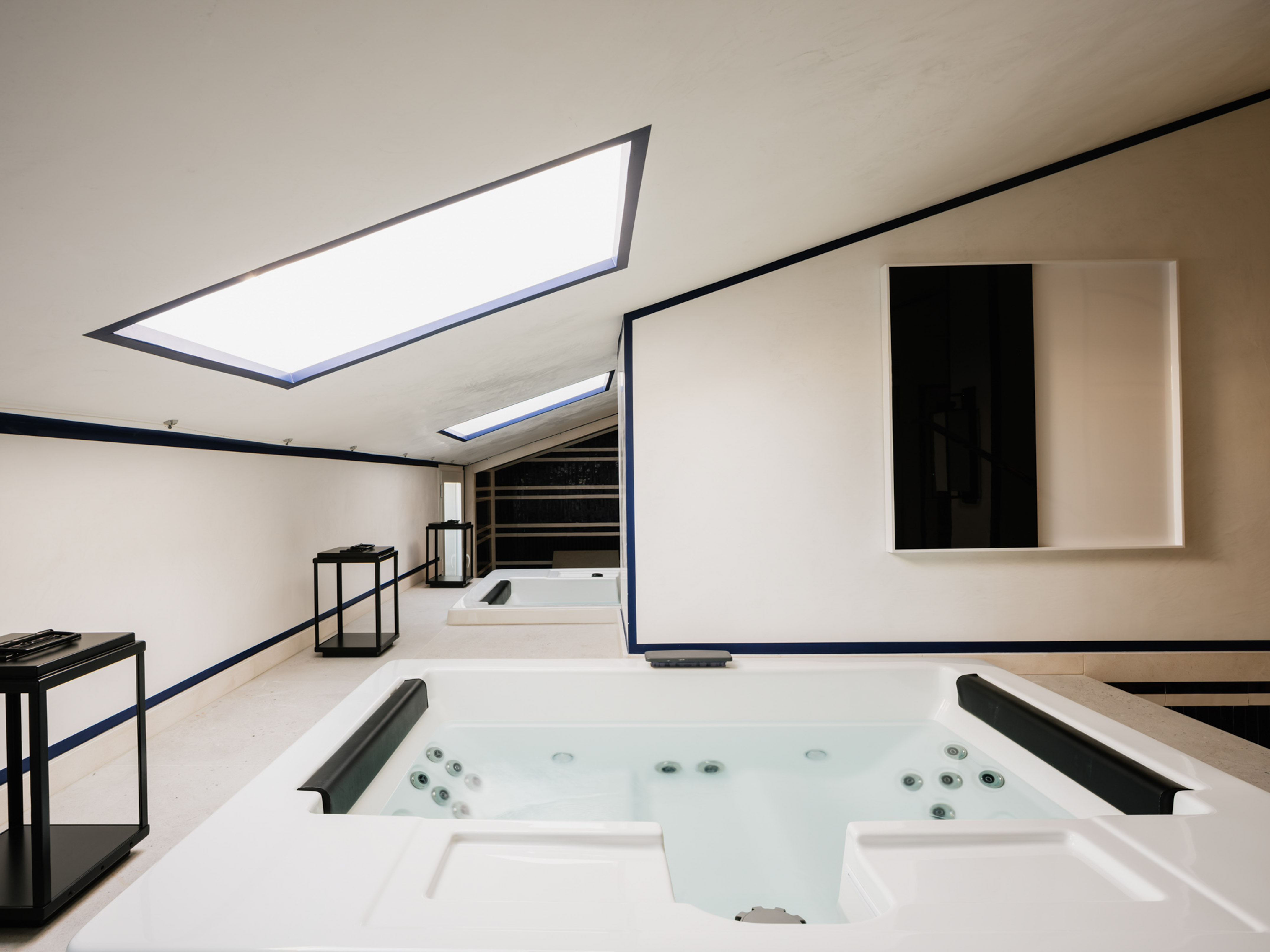 Luxury spa room with white jacuzzis, bright skylights, and blue trim.
