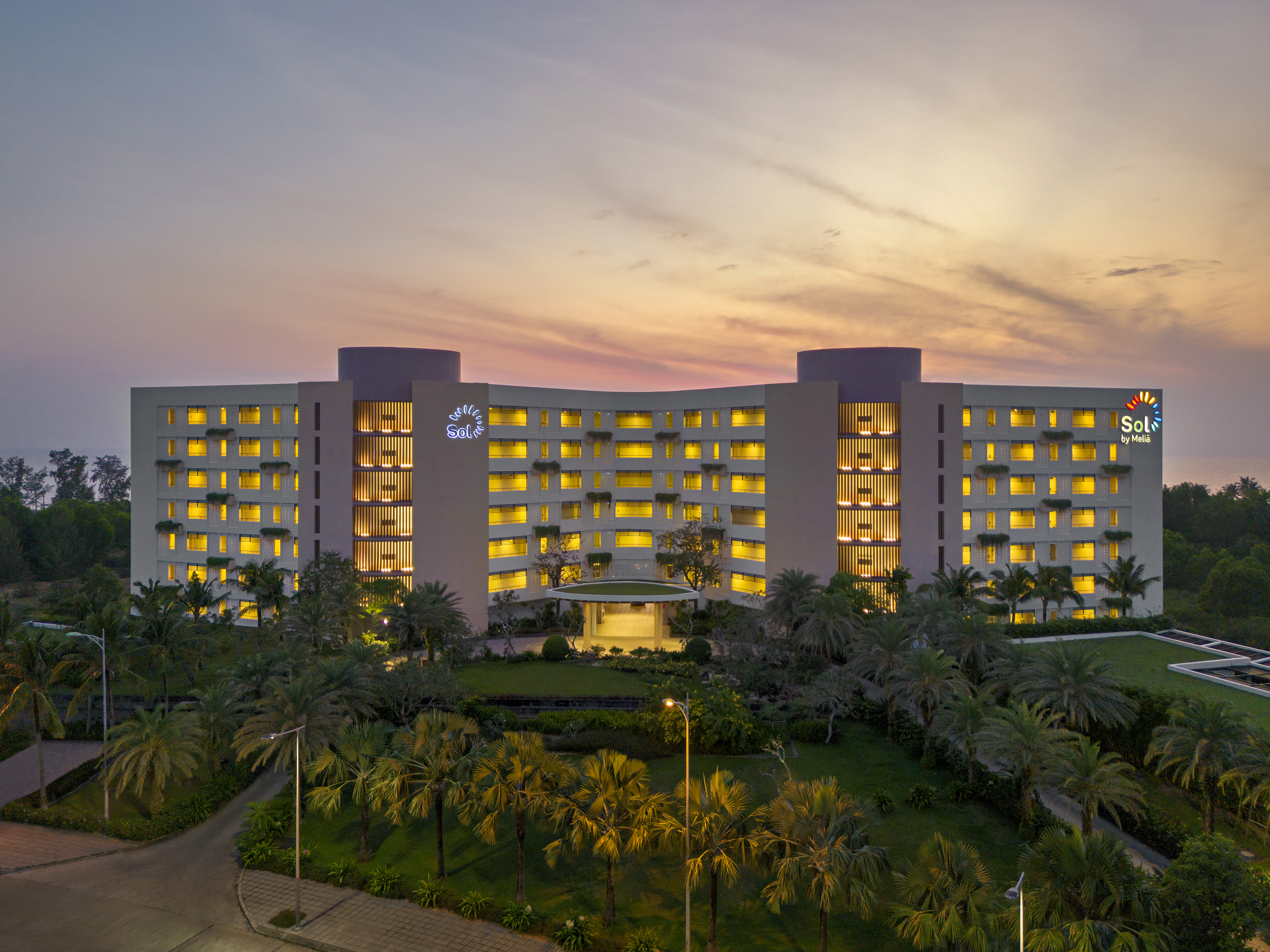 Sol by Meliá hotel illuminated at dusk, surrounded by tropical palm trees.