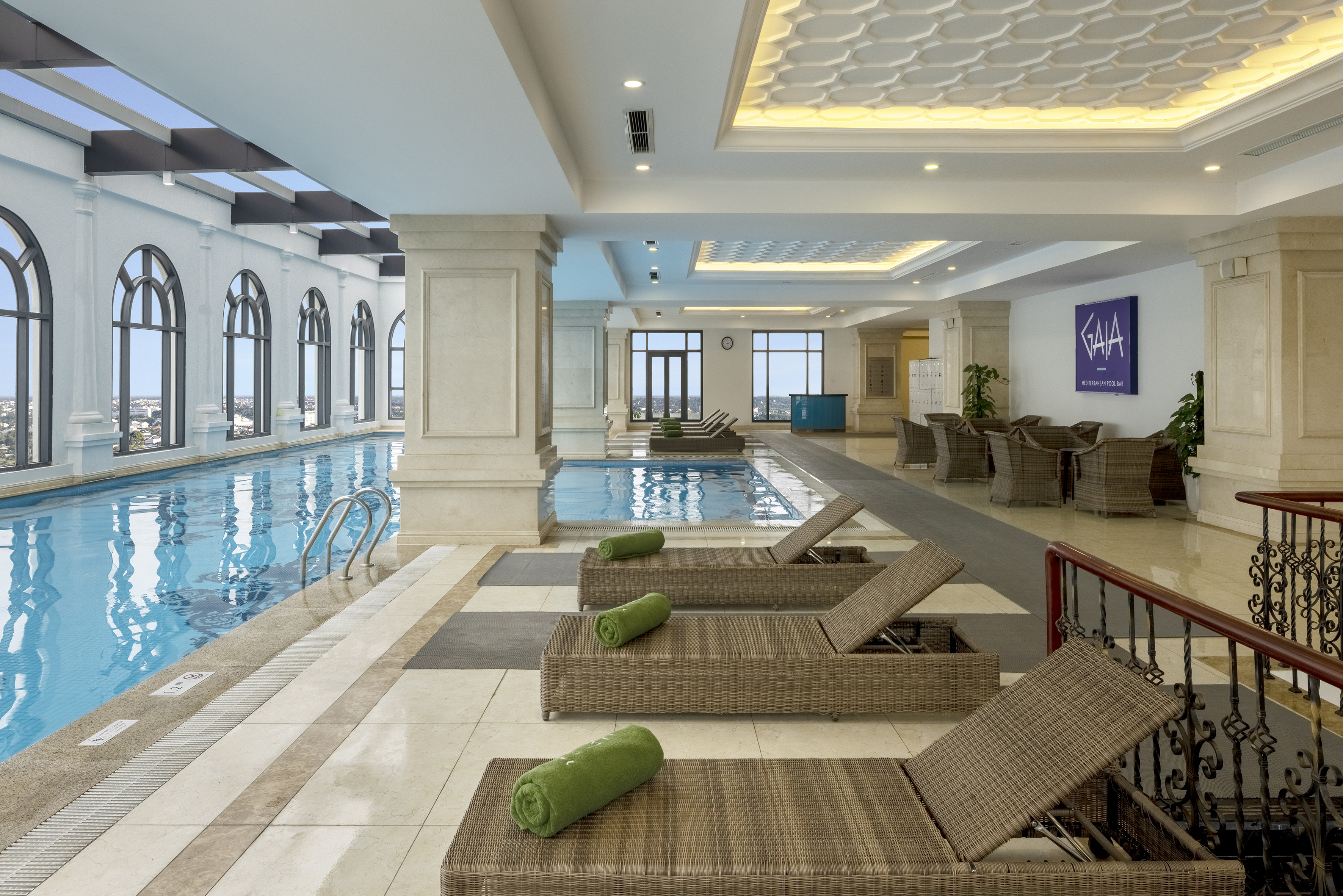 Luxury indoor pool with arched windows, lounge chairs, and hotel pool bar.