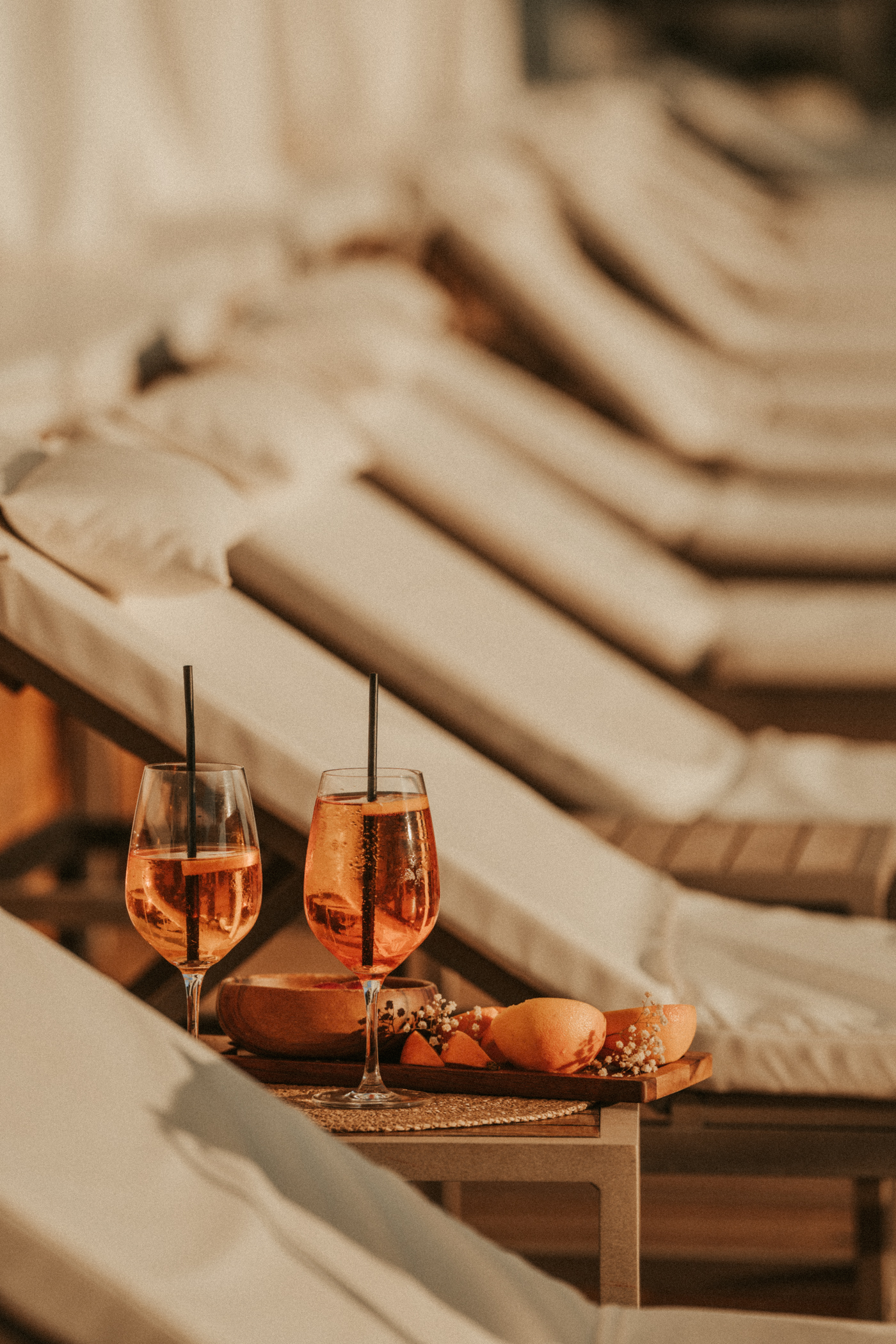 Golden hour Aperol Spritz cocktails with oranges by pool lounge chairs.