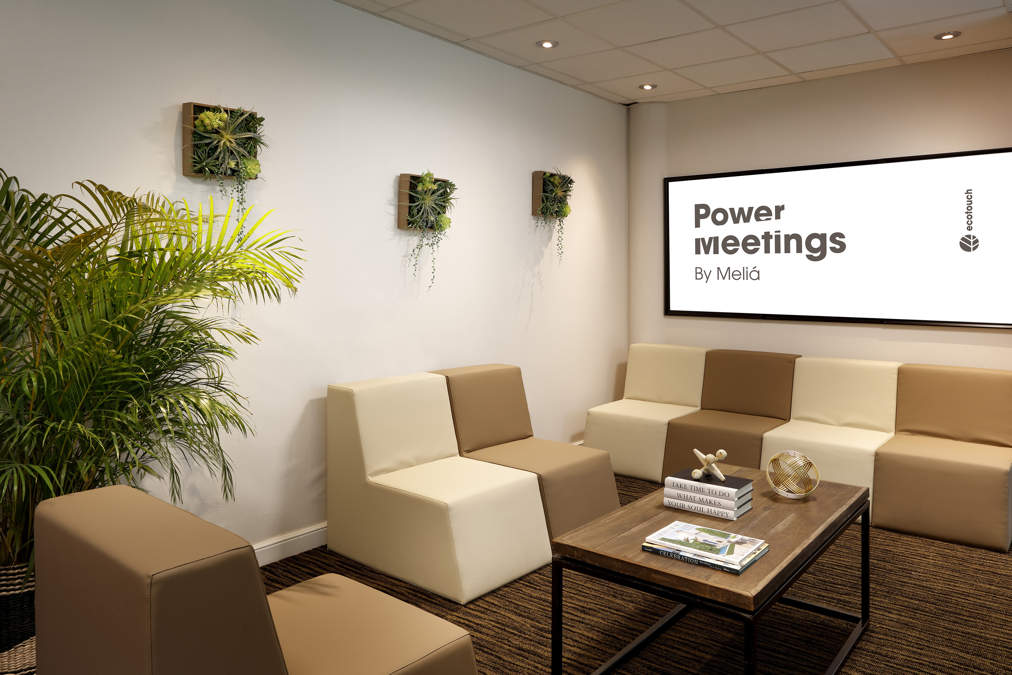 Modern office lounge with modular seating, plants, and "Power meetings" display.