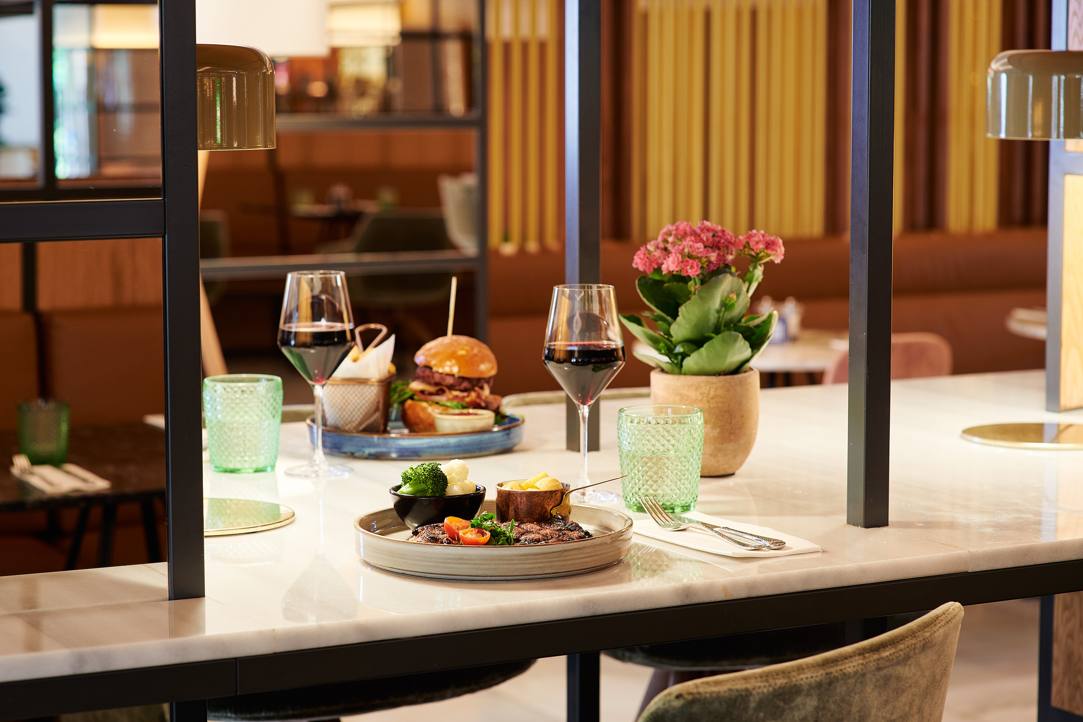 Steak and burger meals with red wine on a modern restaurant counter.