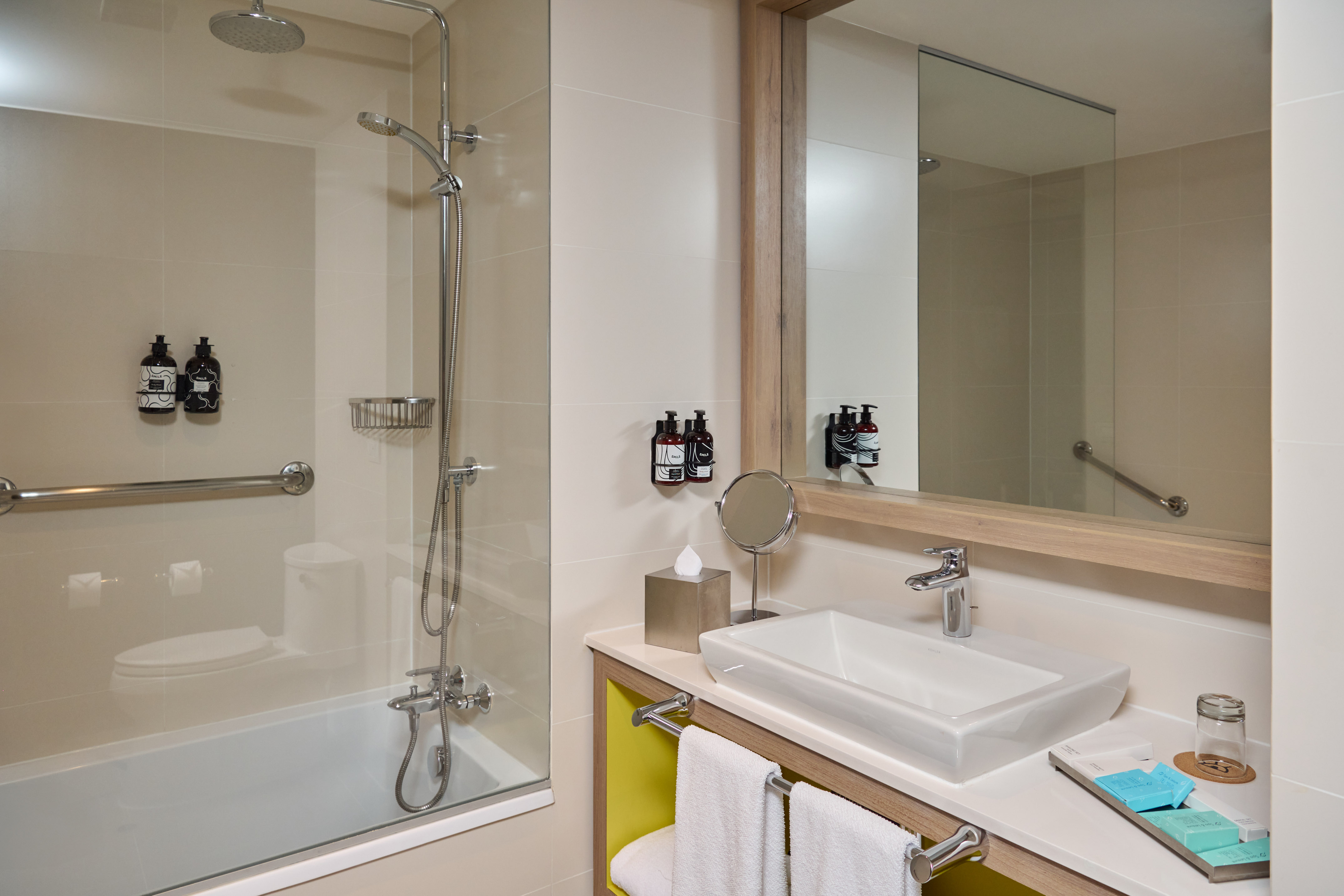 Modern hotel bathroom with shower-tub combo, vanity, and grab bar.