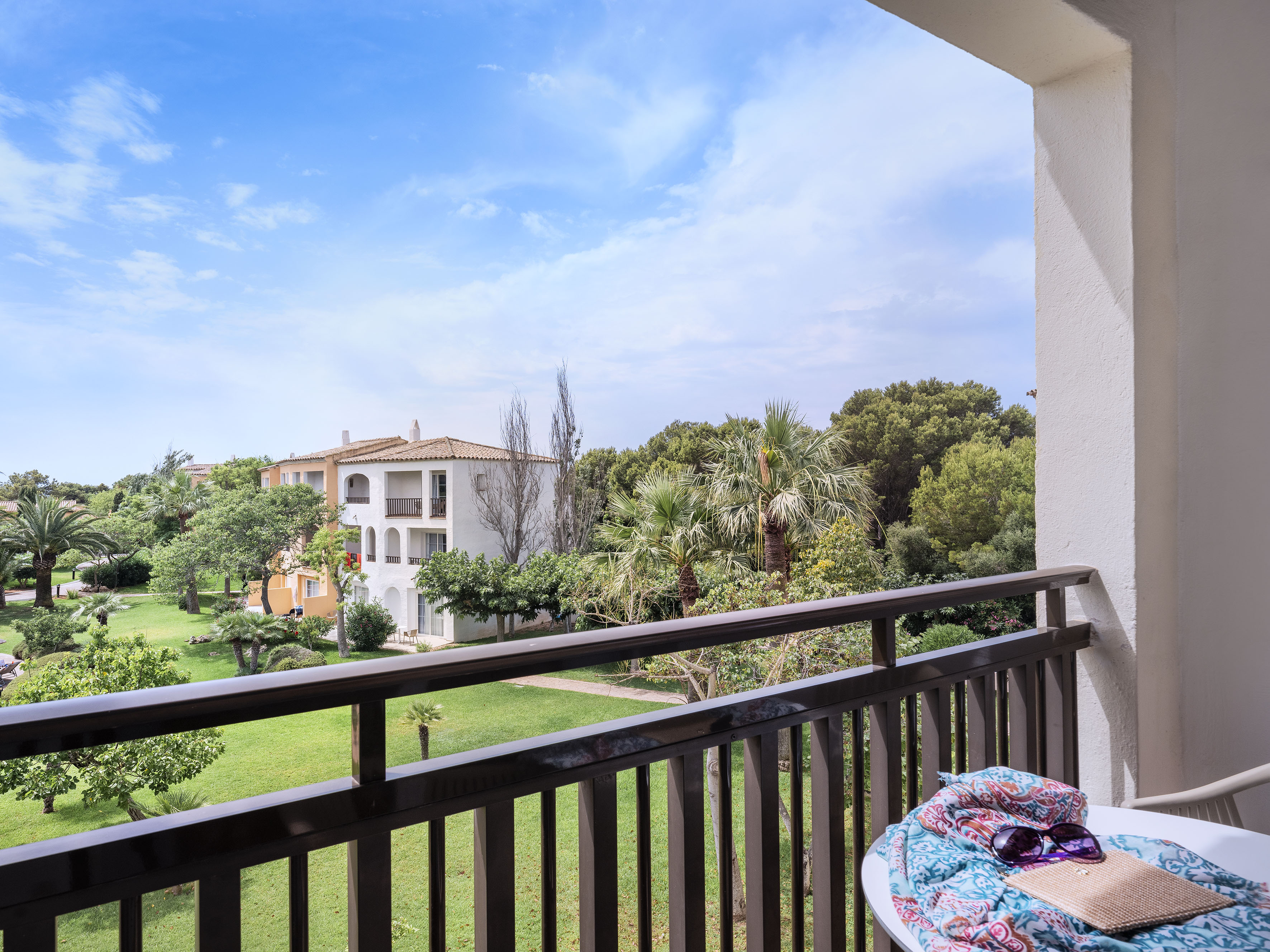 Hotel balcony overlooking resort garden, buildings, with scarf and sunglasses.