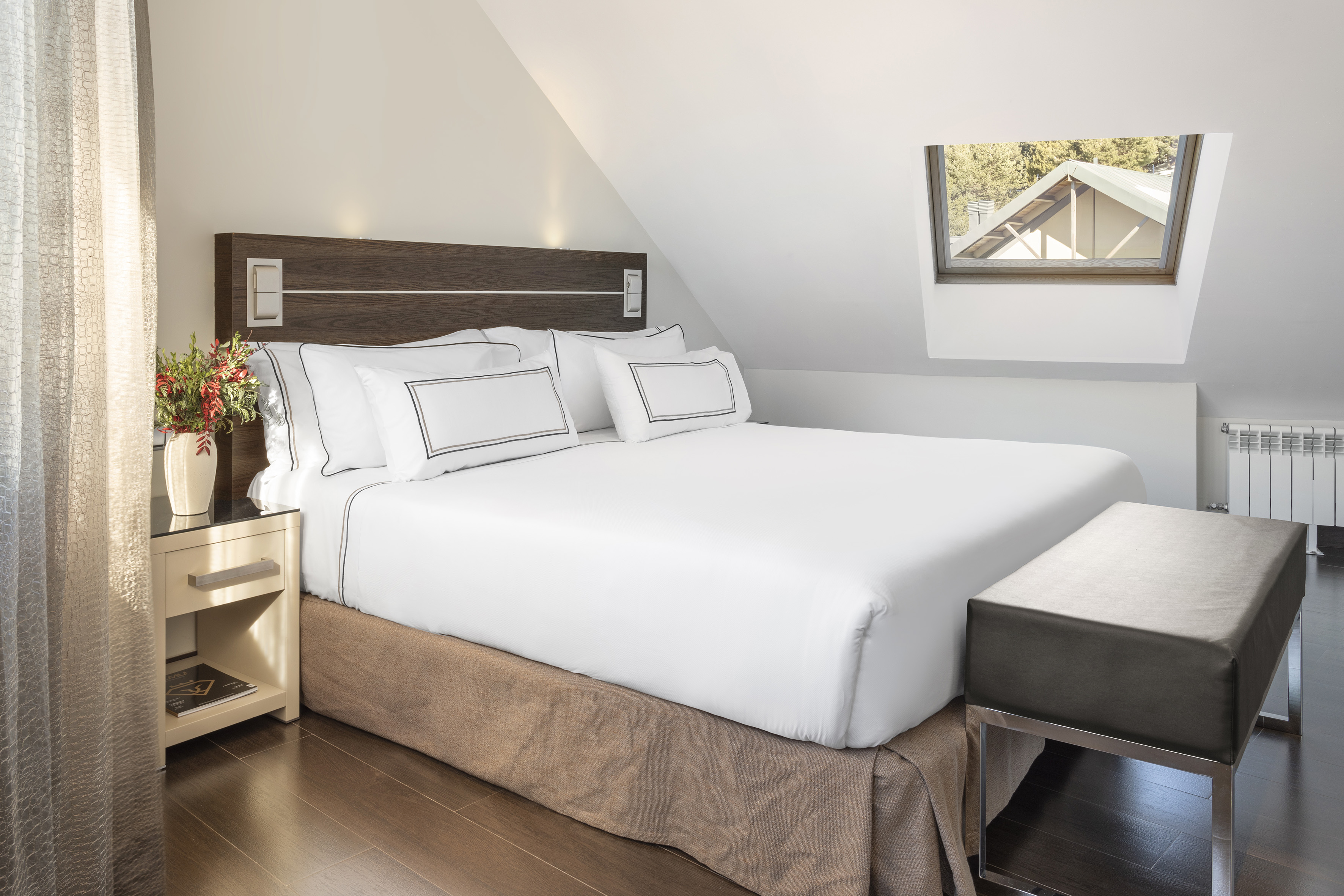Attic hotel bedroom with white bed, wood headboard, and skylight.