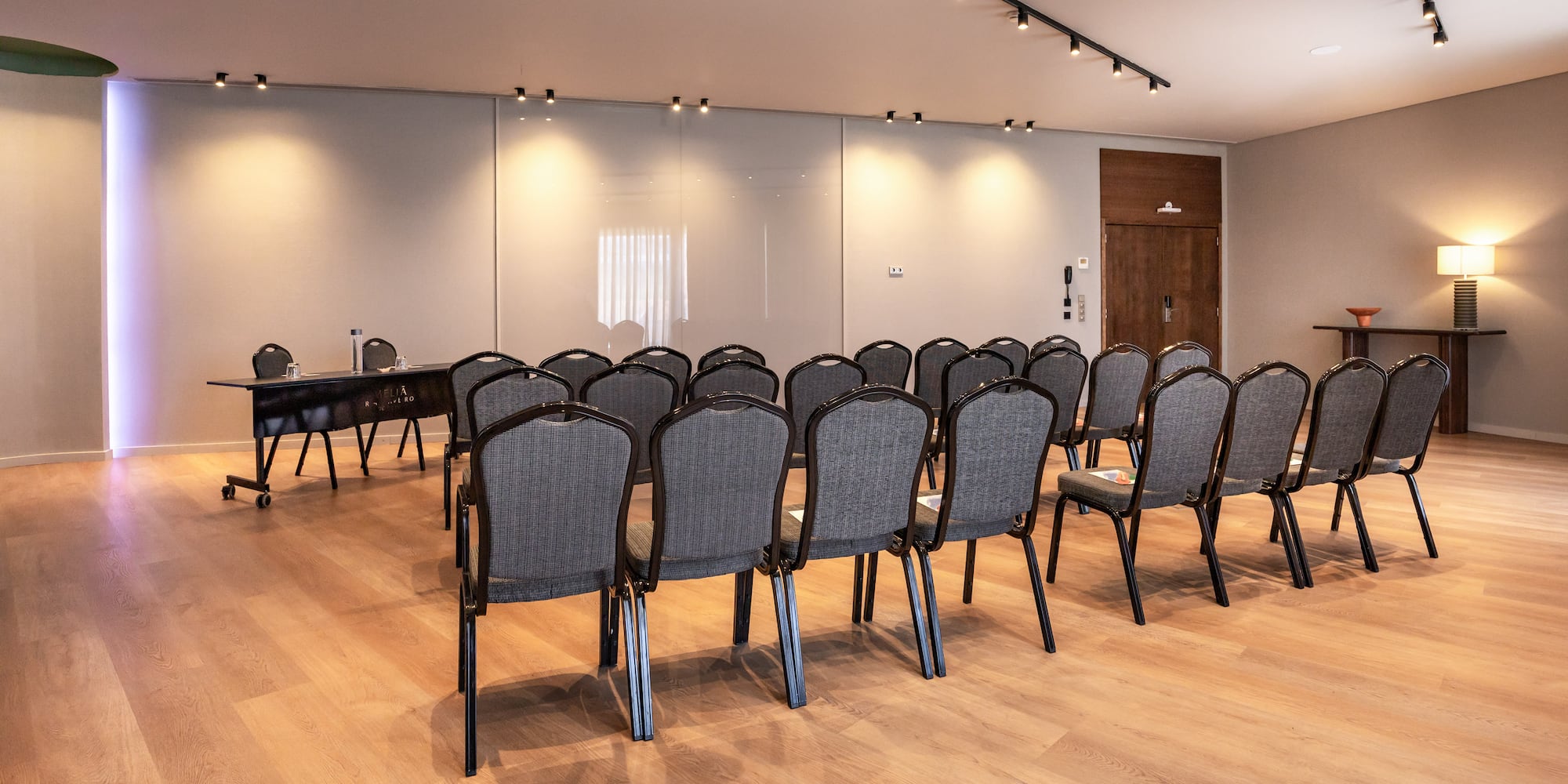 Modern meeting room with rows of gray chairs, wooden floor, and presentation table.