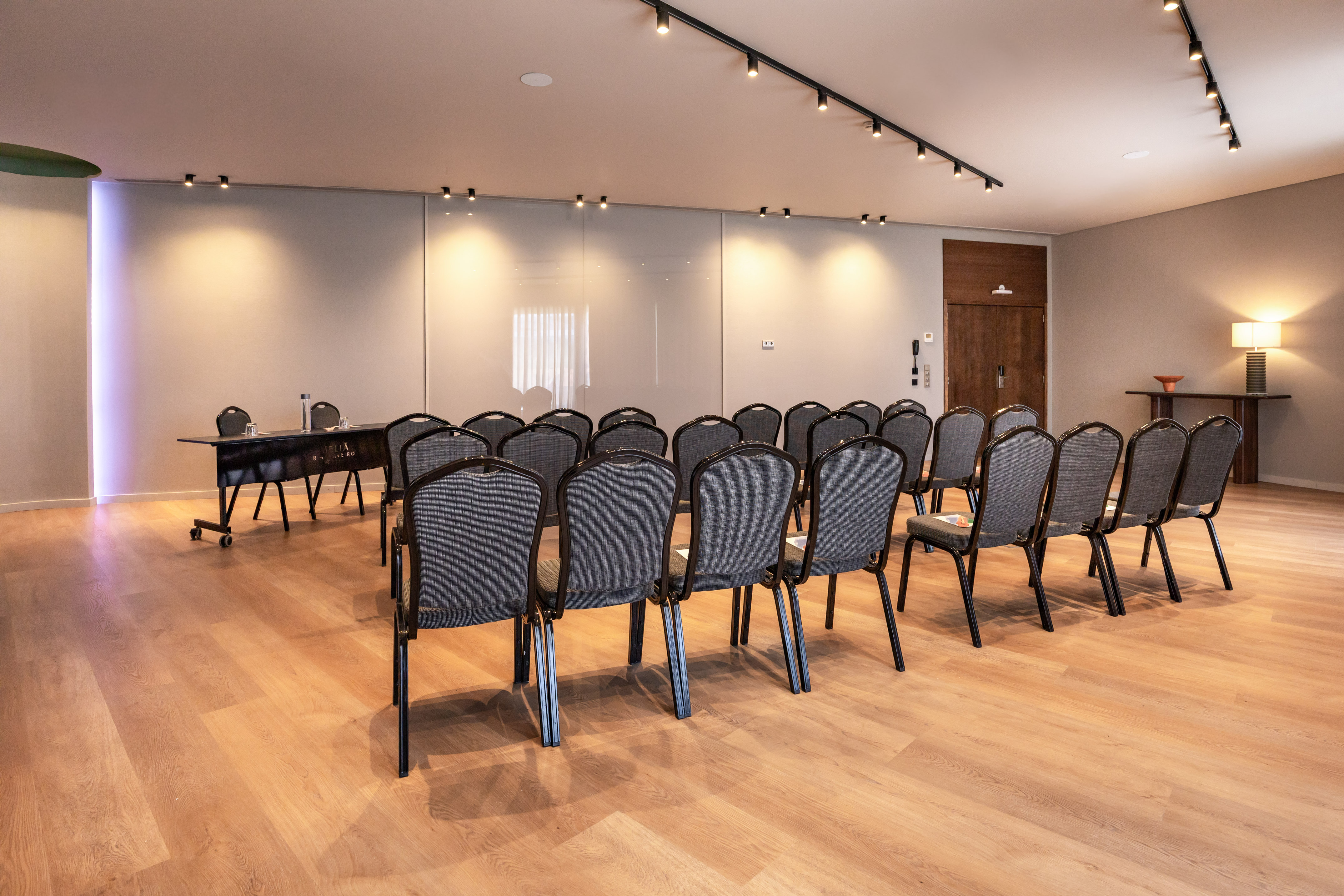 Modern meeting room with rows of gray chairs, wooden floor, and presentation table.