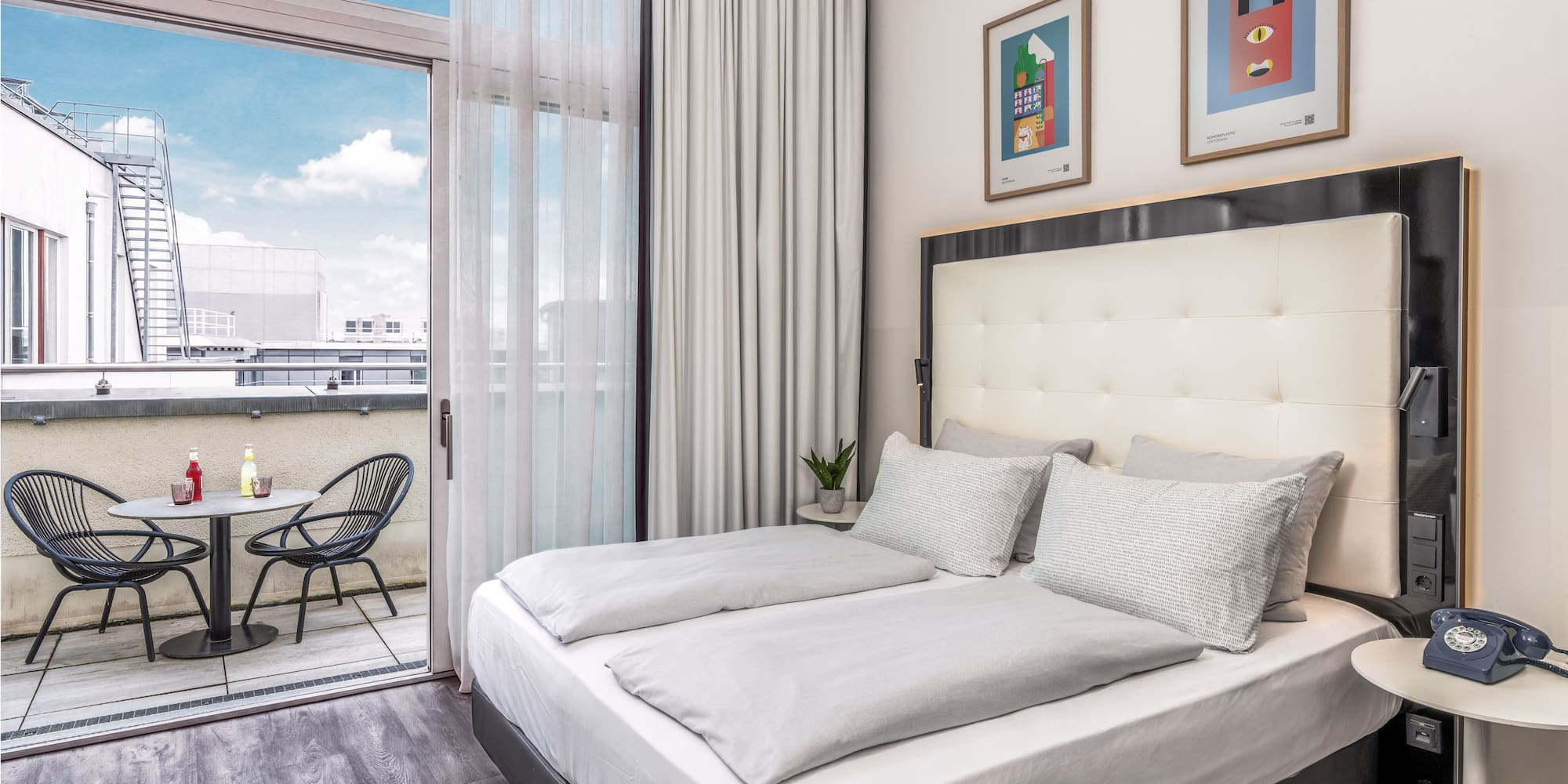 Modern hotel bedroom with large bed, private balcony, and city views.