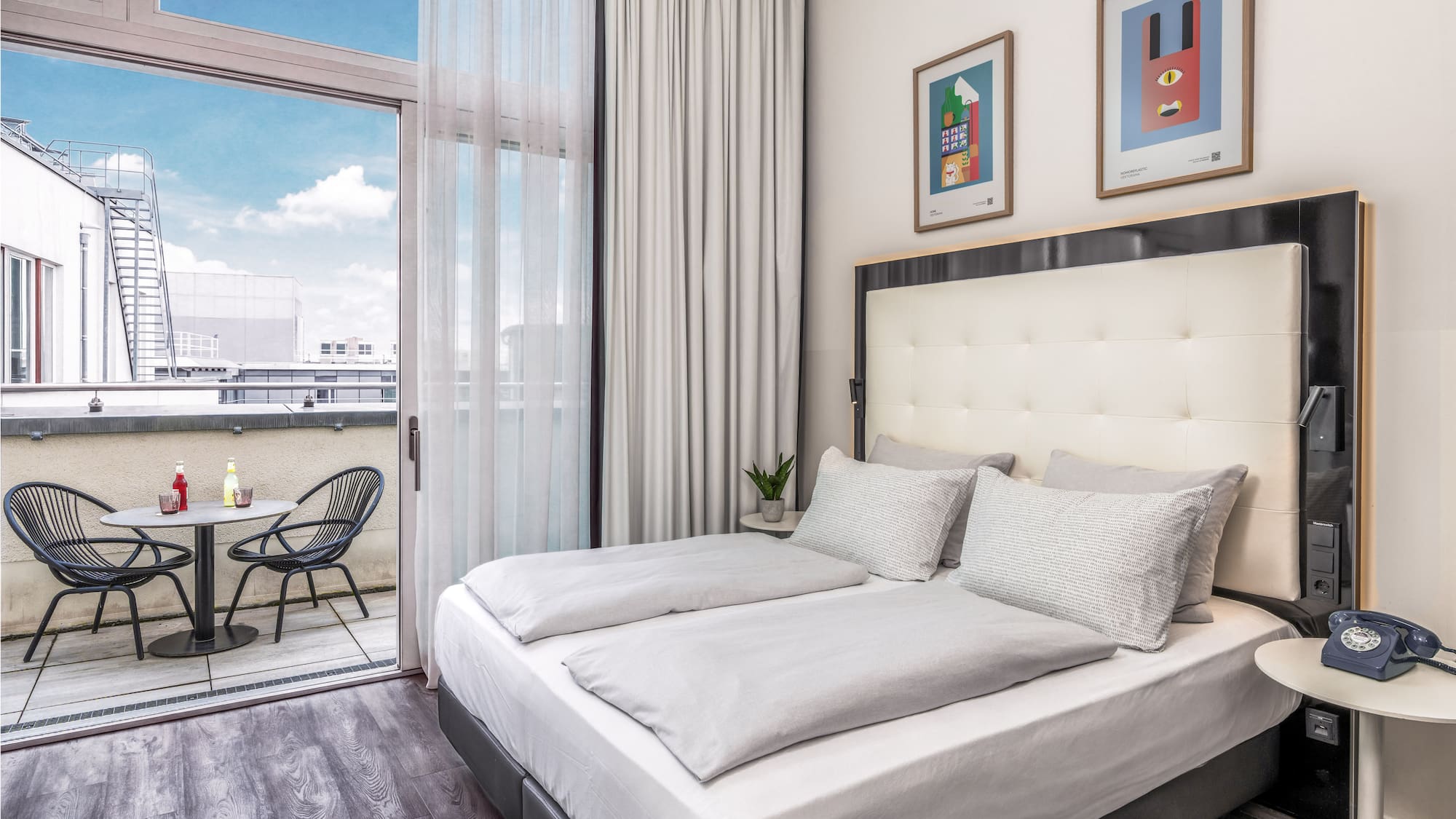 Modern hotel bedroom with large bed, private balcony, and city views.