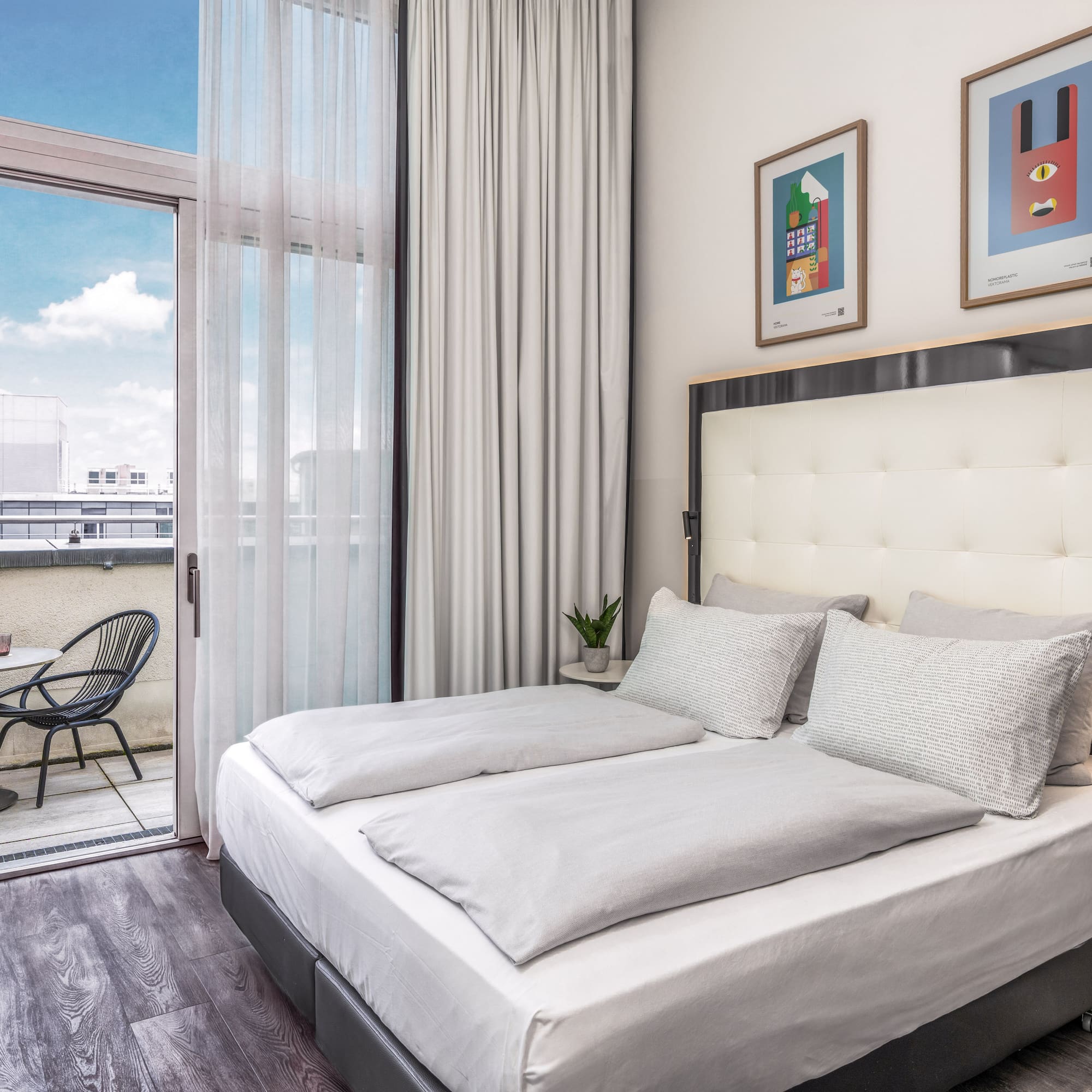 Modern hotel bedroom with large bed, private balcony, and city views.