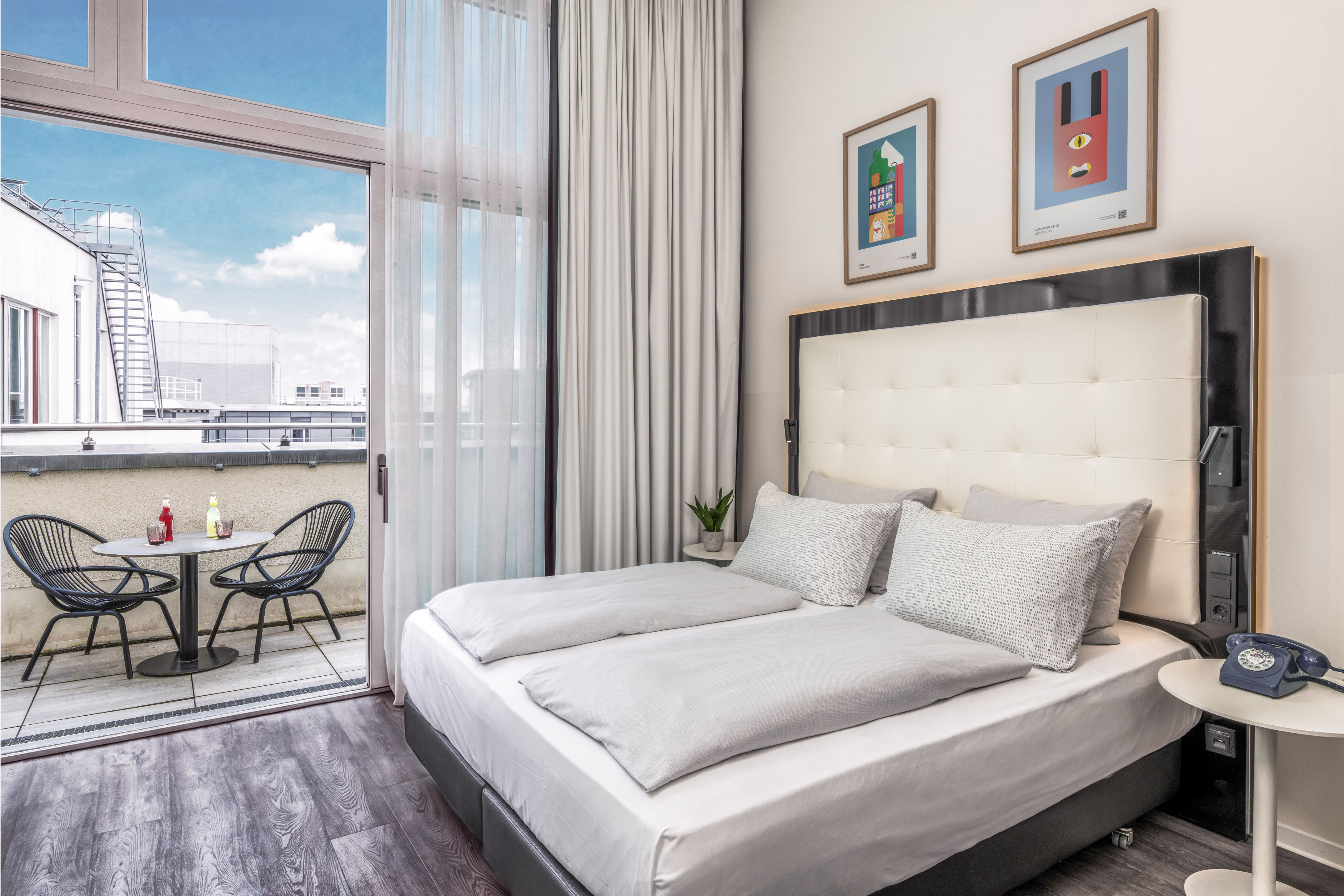 Modern hotel bedroom with large bed, private balcony, and city views.
