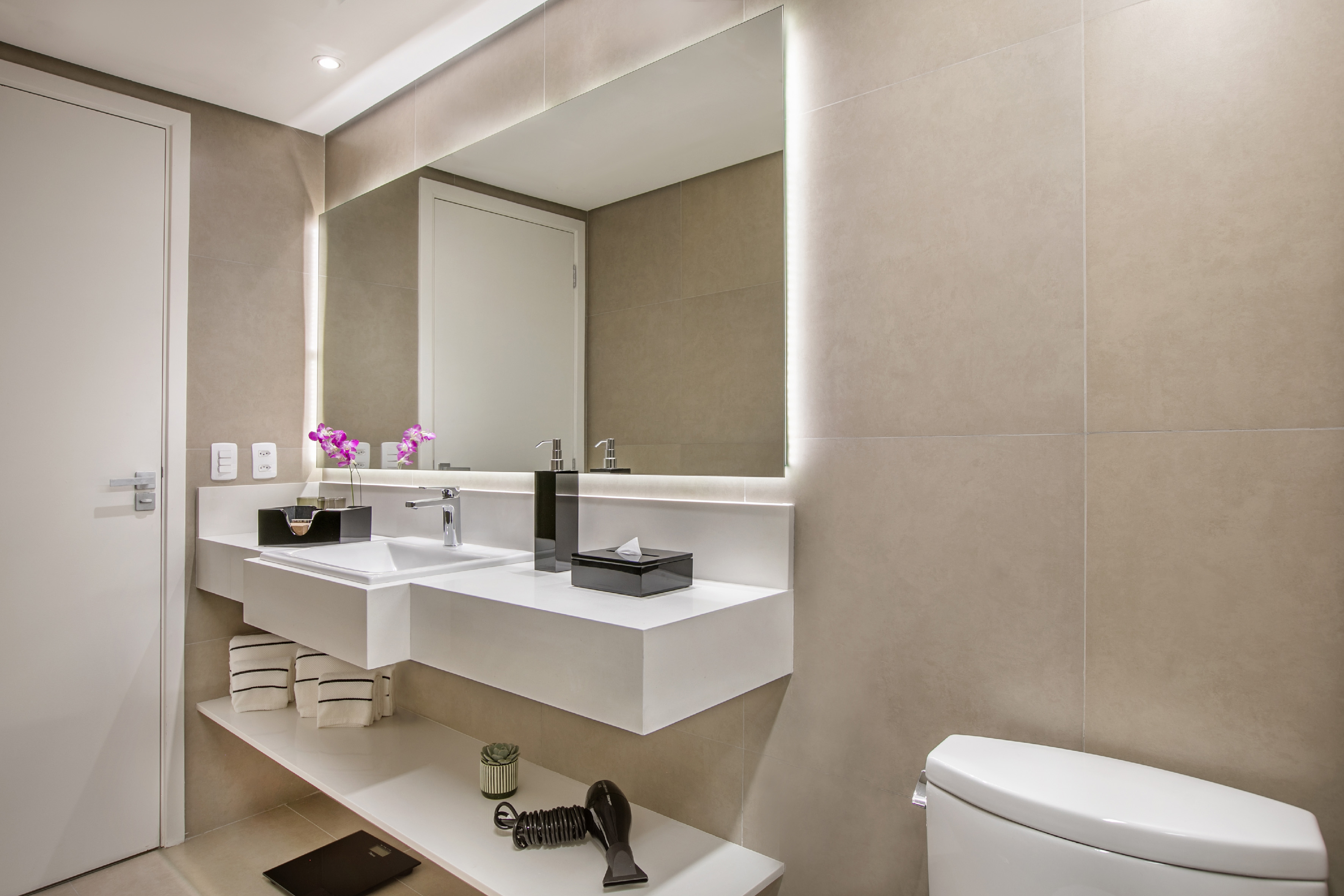 Contemporary bathroom vanity with backlit mirror, white sink, beige tiles.