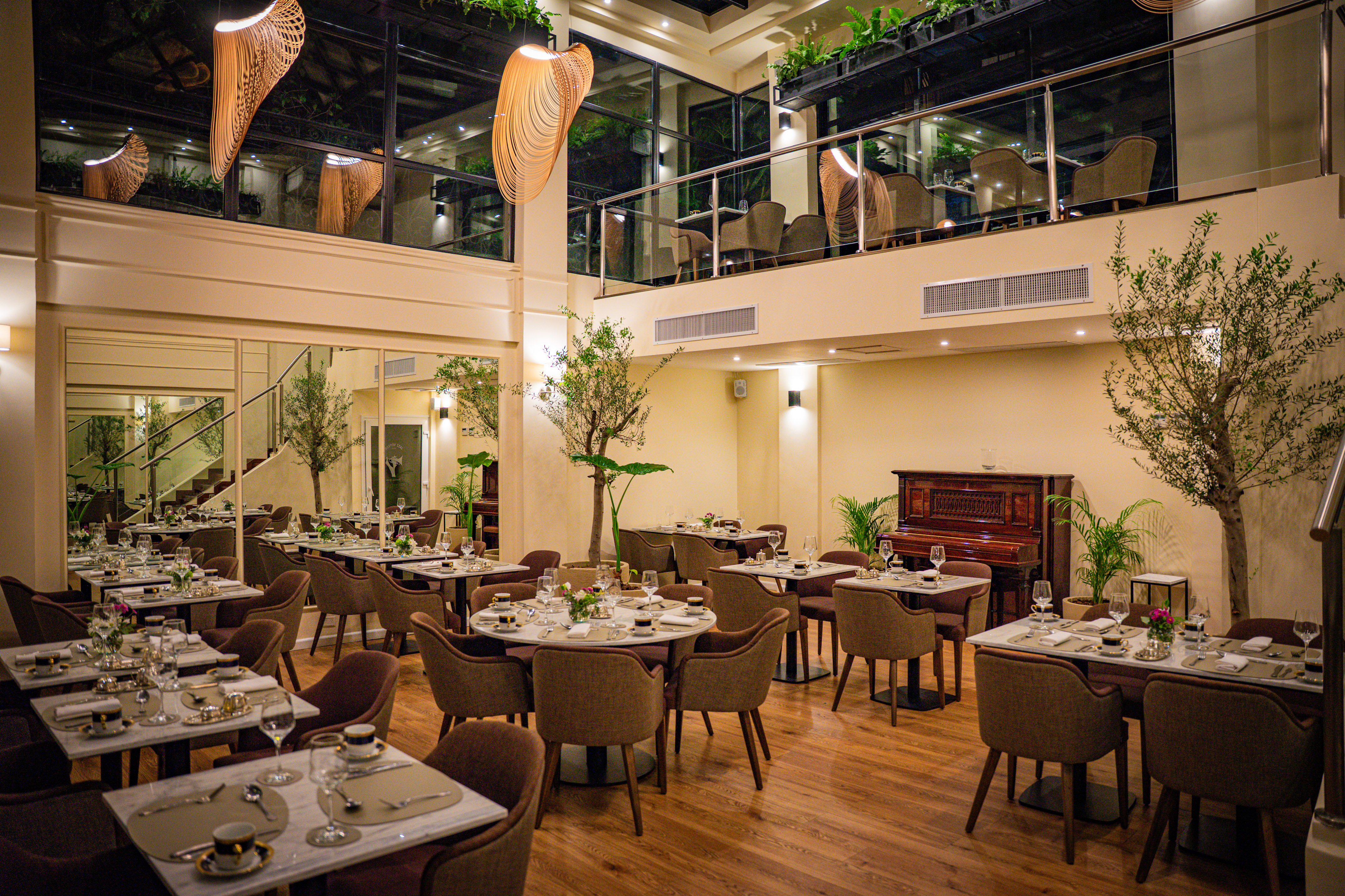 Elegant multi-level restaurant with set dining tables, modern decor, and plants.