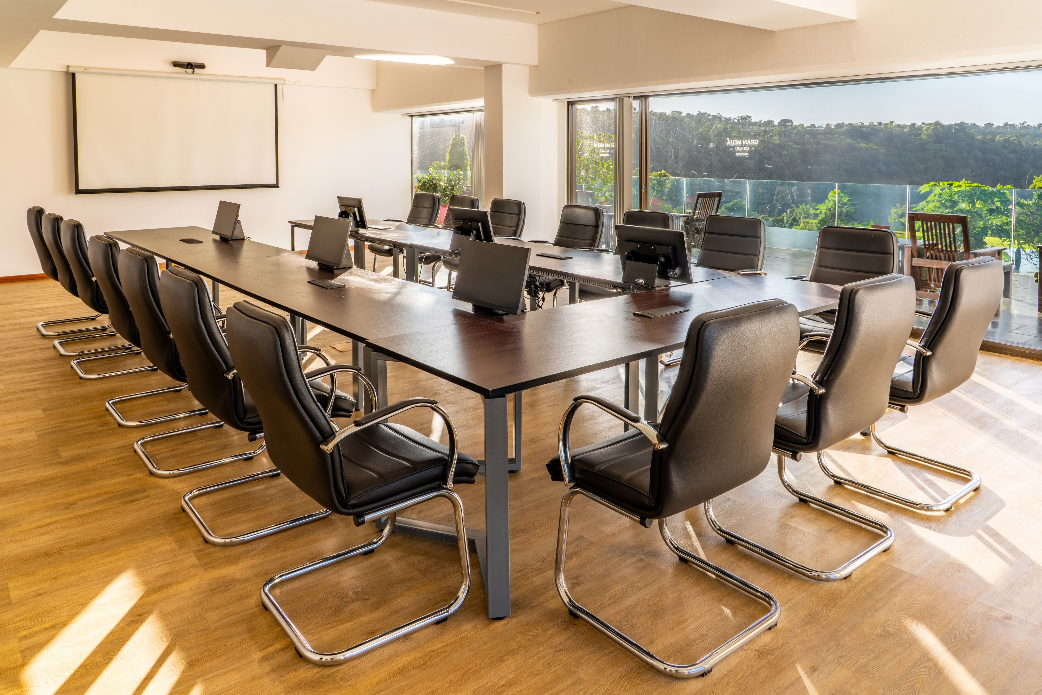 Modern conference room with long table, monitors, projection screen, and window view.