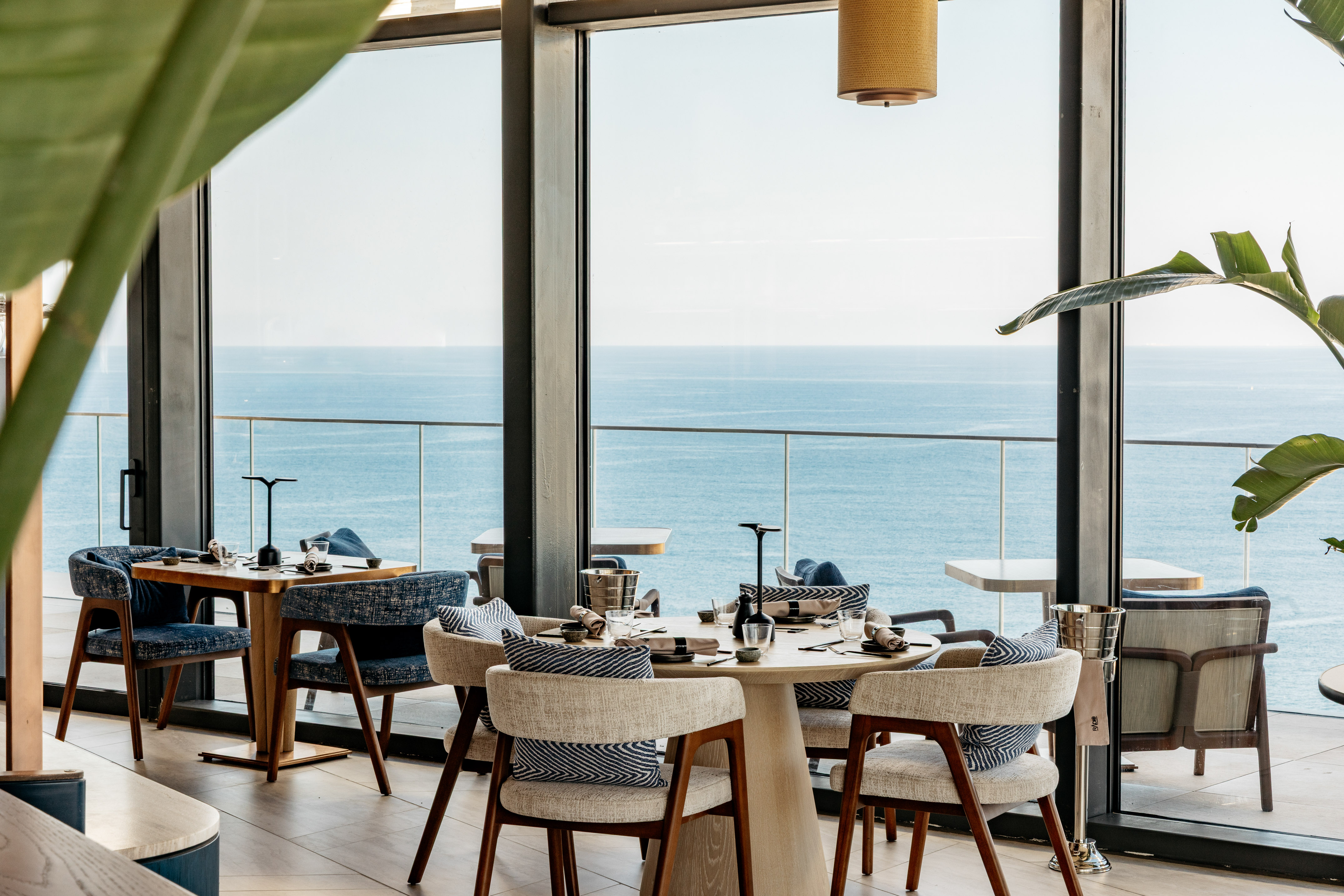 Modern restaurant with ocean view, elegant tables, and contemporary interior.