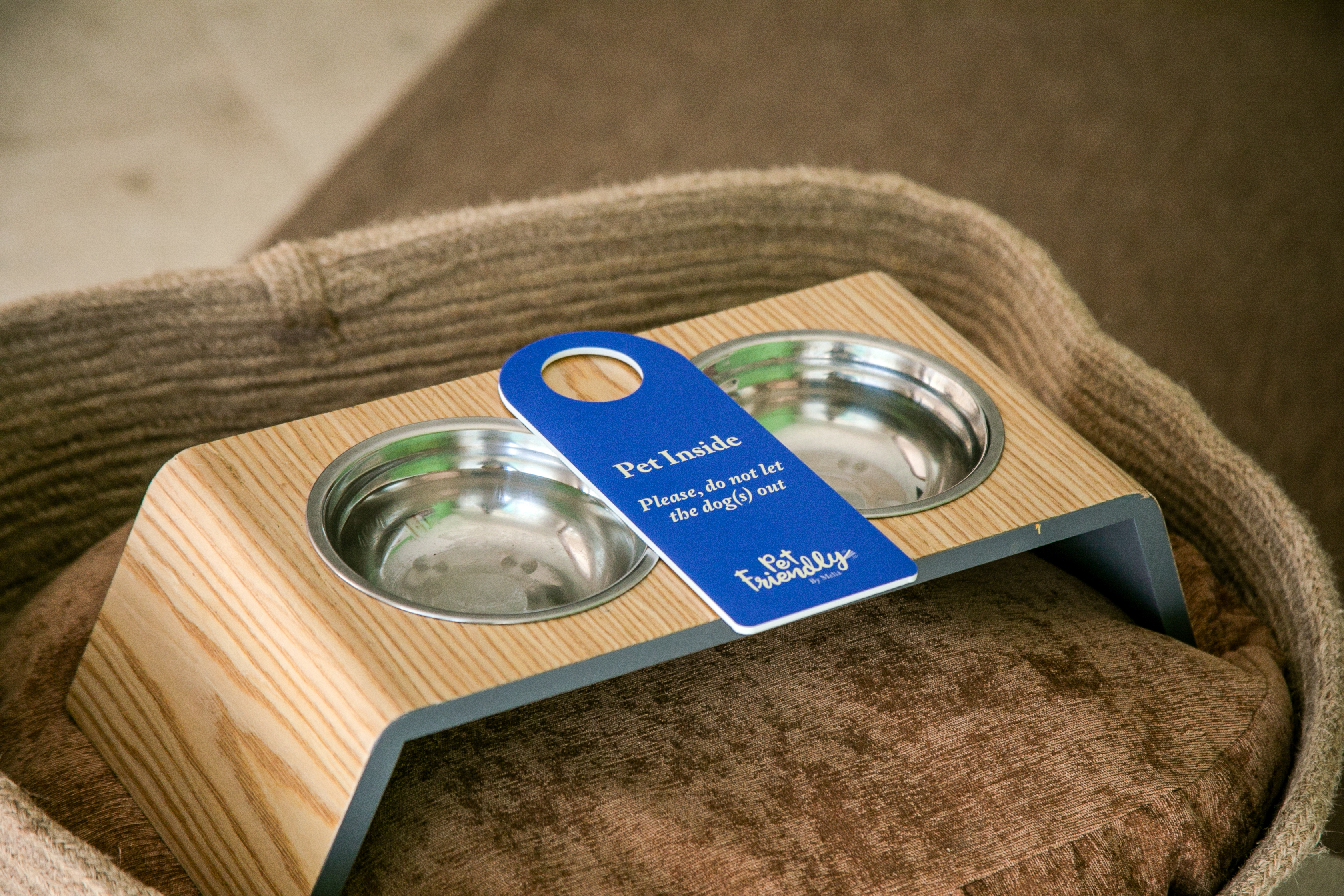 Pet friendly hotel dog bowls in wooden feeder with "Pet Inside" door tag.
