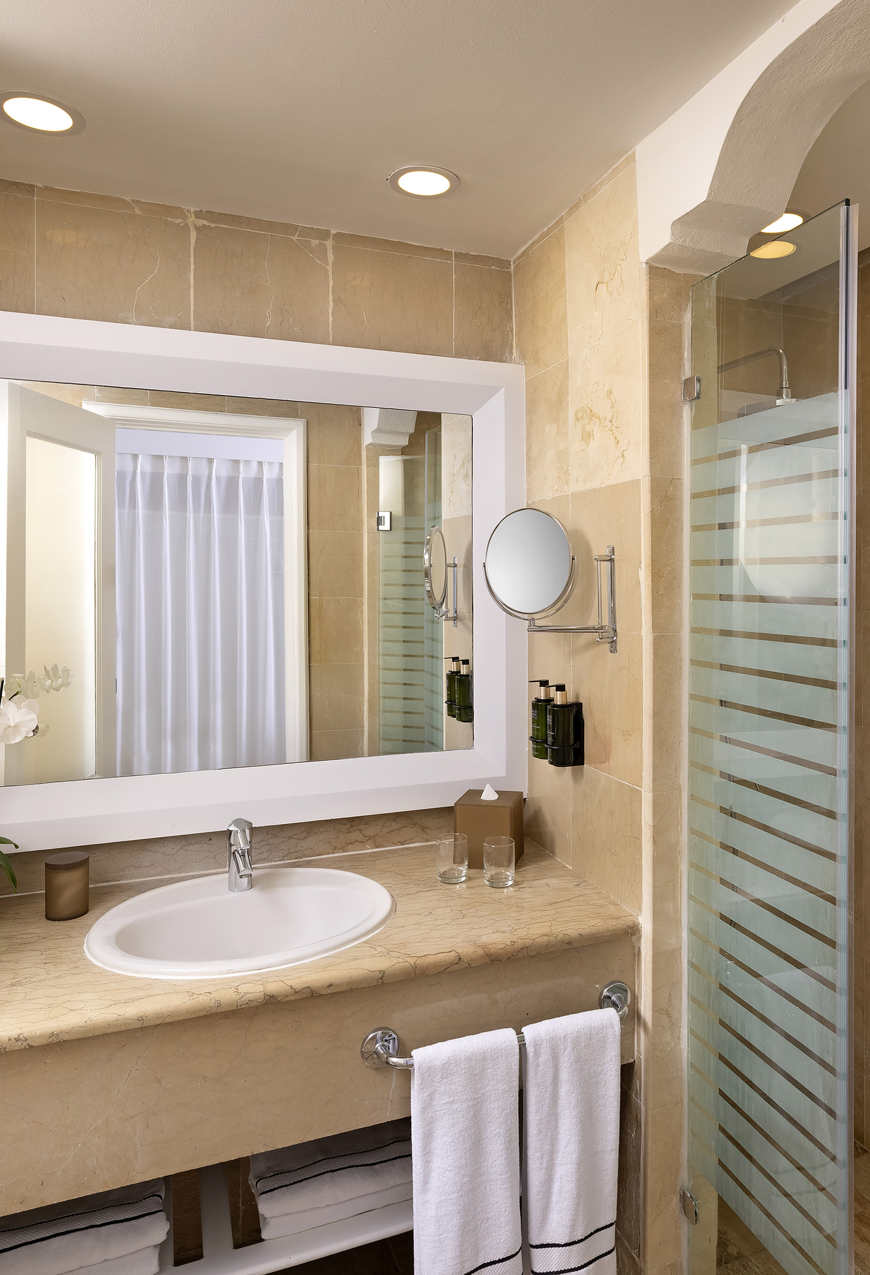 Modern marble bathroom with sink, mirror, glass shower, and white towels.