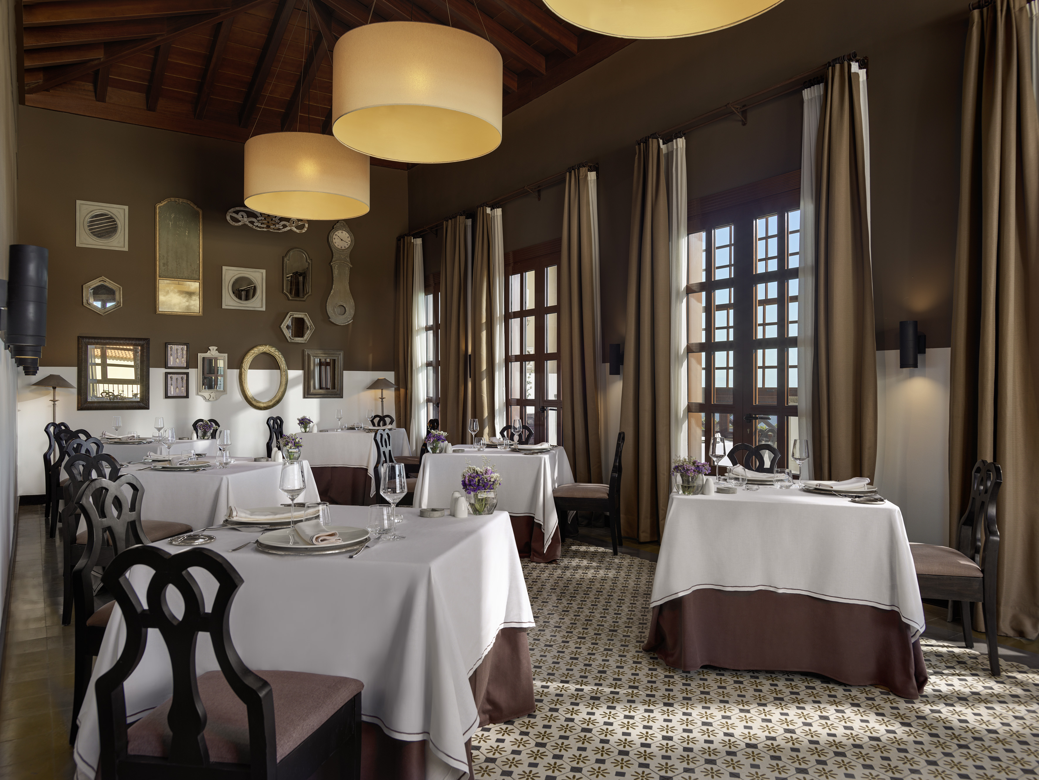 Elegant restaurant dining room with set tables, ornate mirrors, and patterned floor.