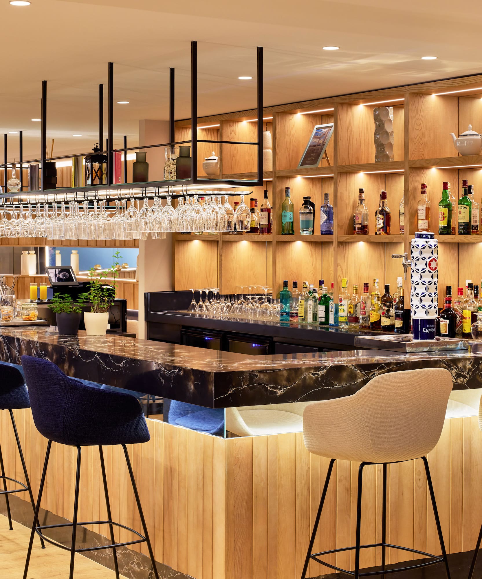 Bar de hotel moderno con mostrador de mármol y madera, taburetes y bebidas.