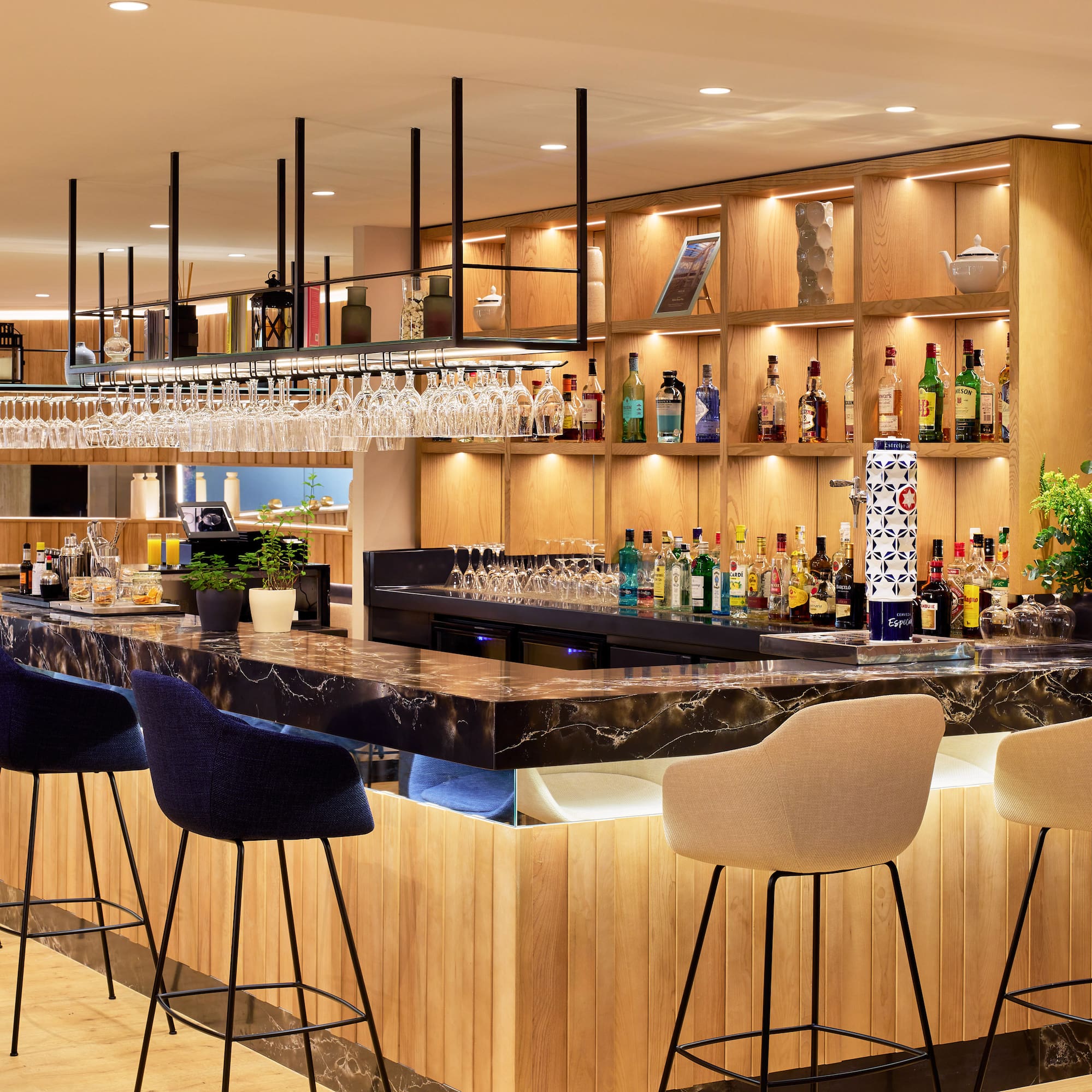 Bar moderno con barra de mármol negro, estantes de madera iluminados y taburetes.