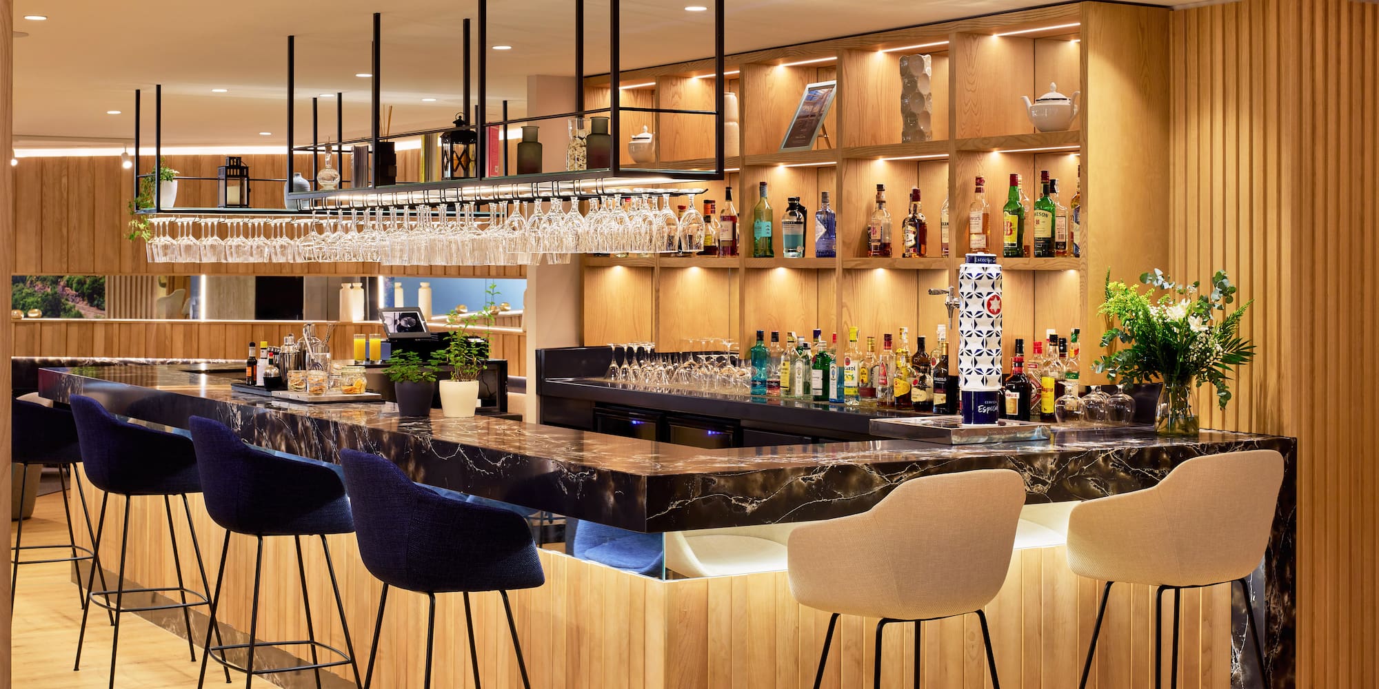 Bar de hotel moderno: barra de mármol, botellas de licor, taburetes y madera.