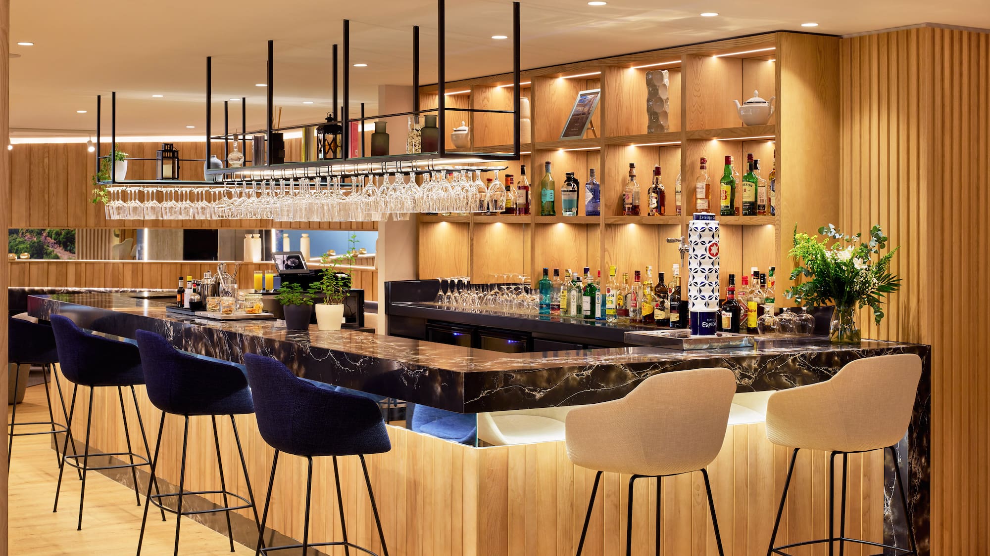 Bar de hotel moderno: barra de mármol, botellas de licor, taburetes y madera.