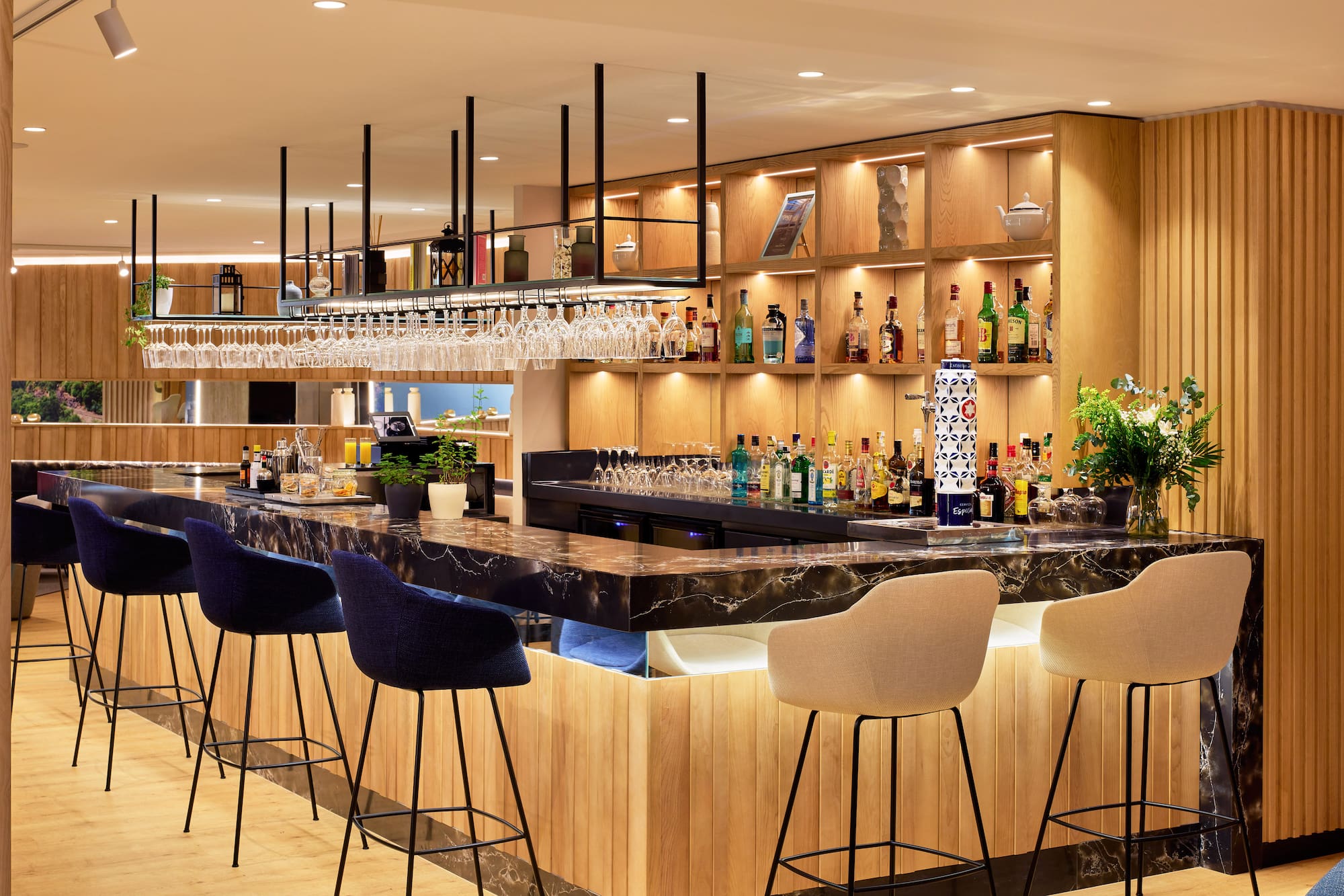 Bar de hotel moderno con mostrador de mármol, madera, taburetes y bebidas.