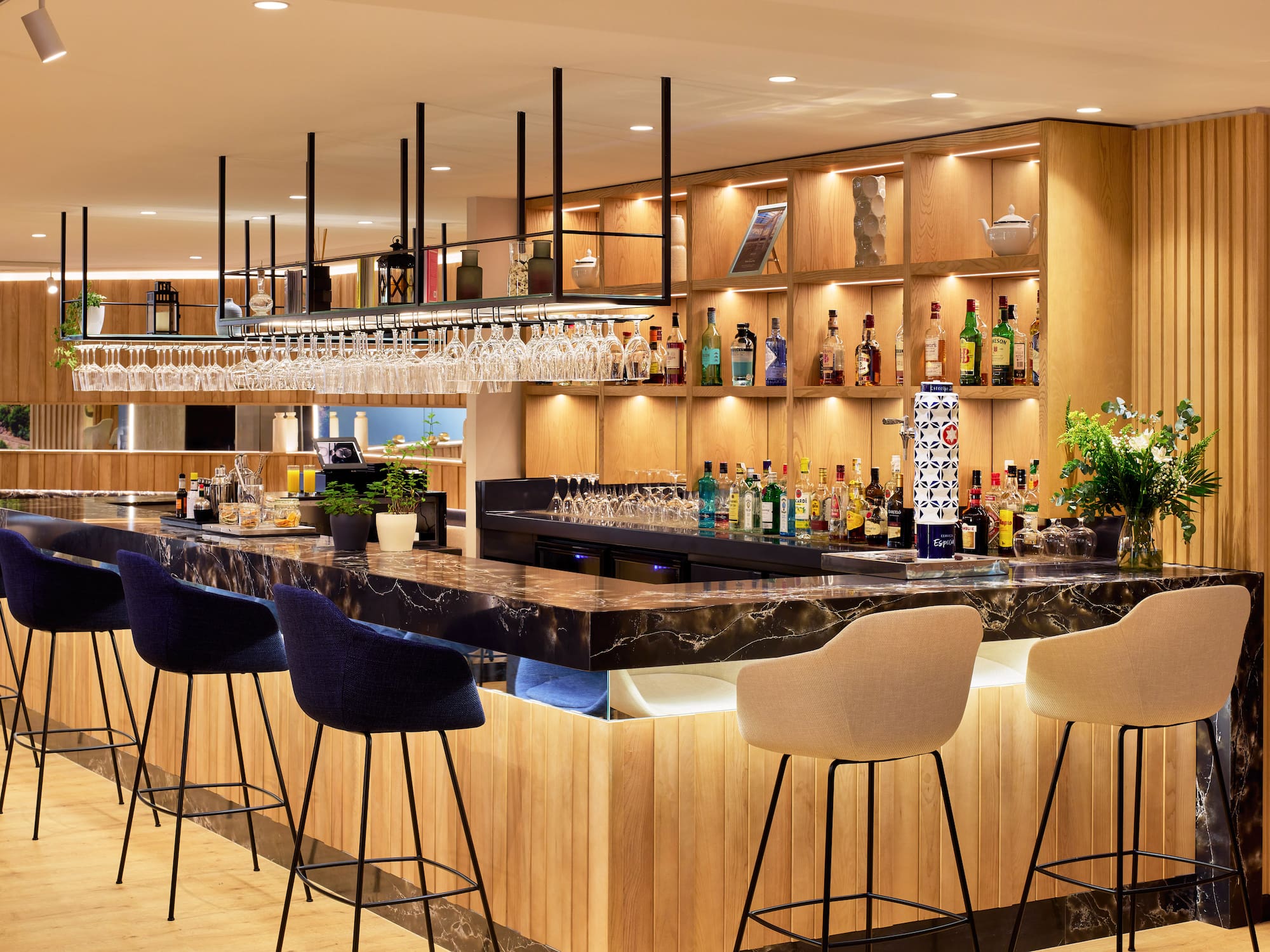 Bar moderno con barra de mármol negro, estantes de madera iluminados y taburetes.