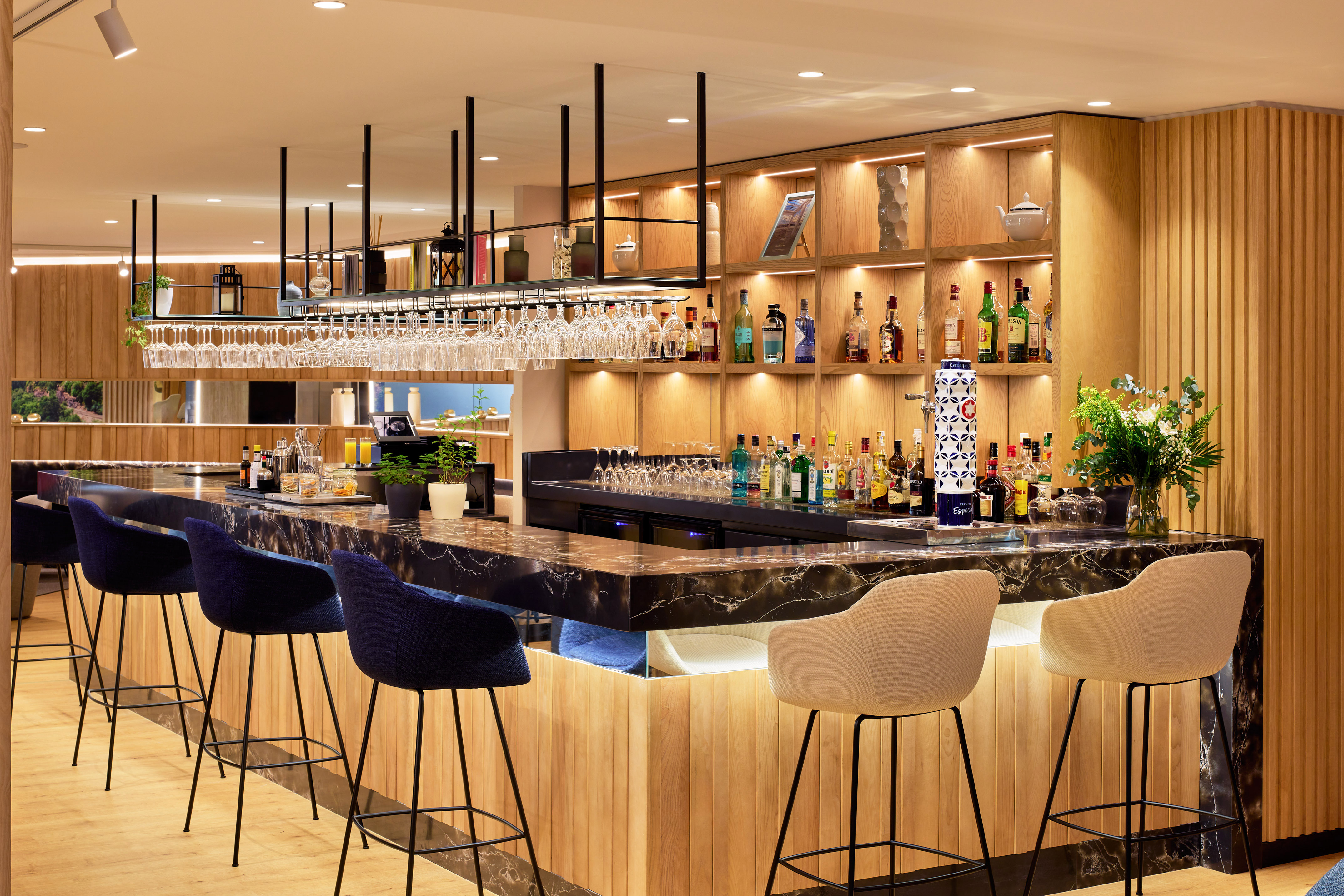 Bar de hotel moderno con mostrador de mármol, madera, taburetes y bebidas.