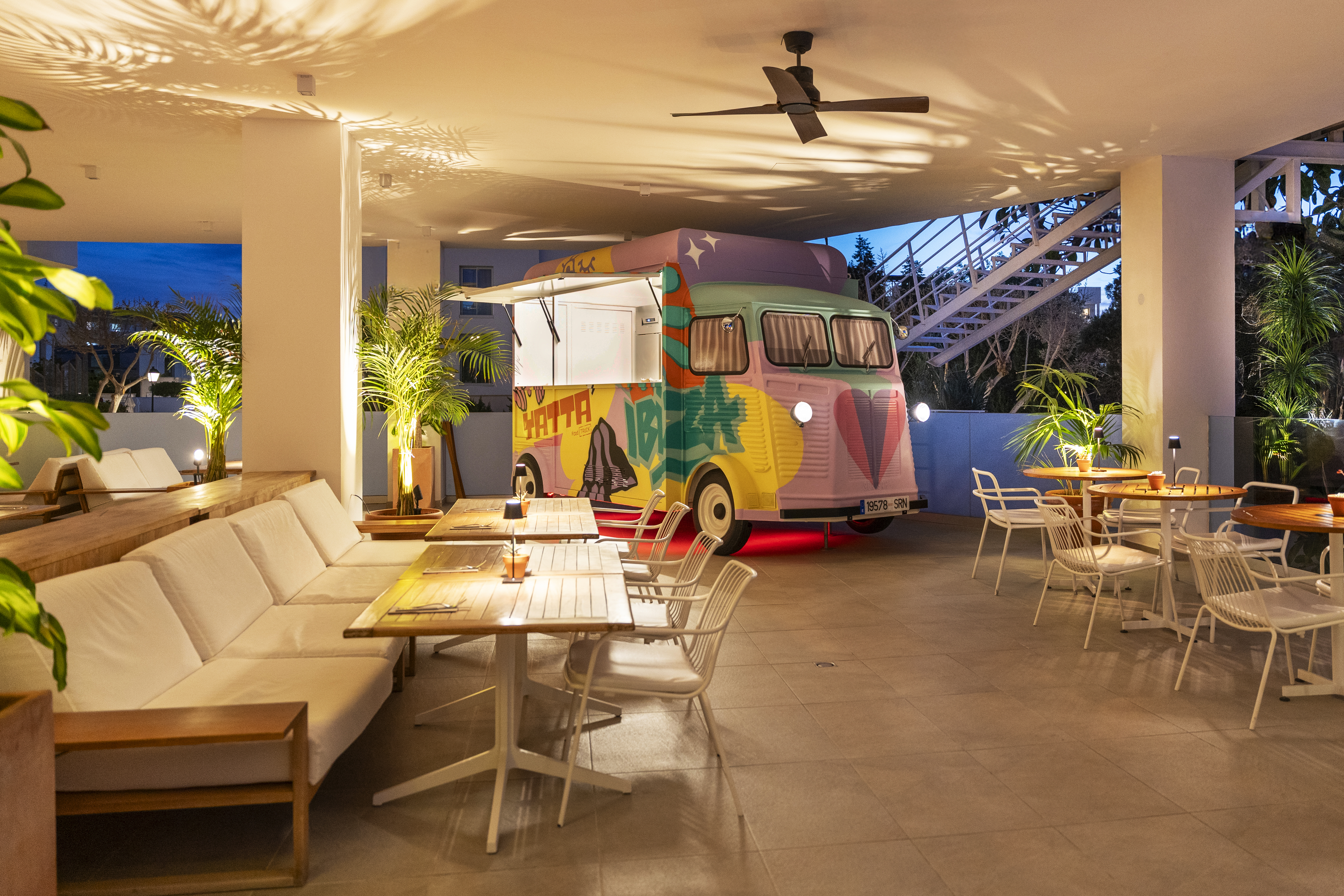 Colorful food truck at modern outdoor restaurant with lounge seating & palm trees.