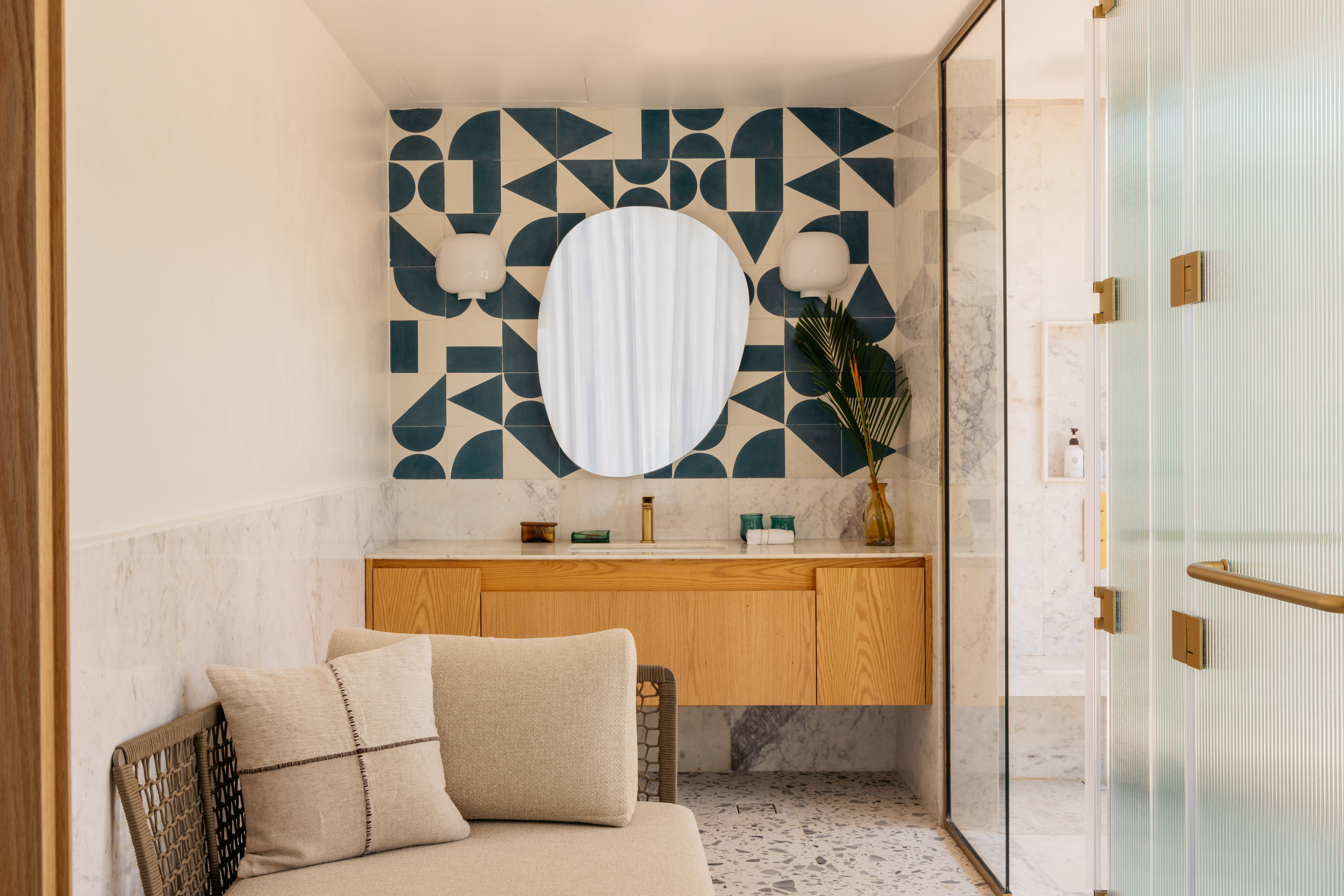 Modern bathroom with blue geometric tiles, wooden vanity, and oval mirror.