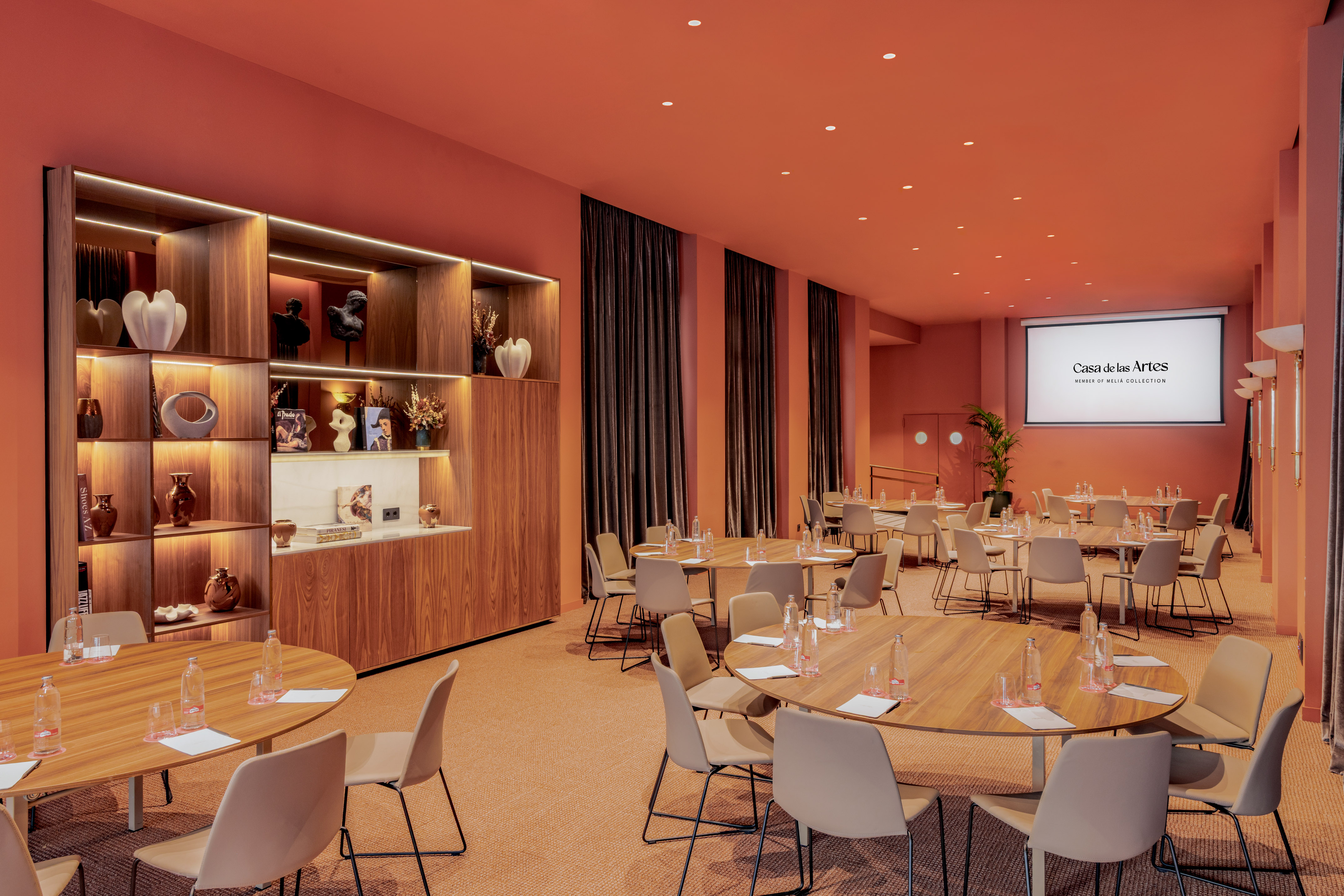Casa de las Artes meeting room with orange decor, round tables, and screen.