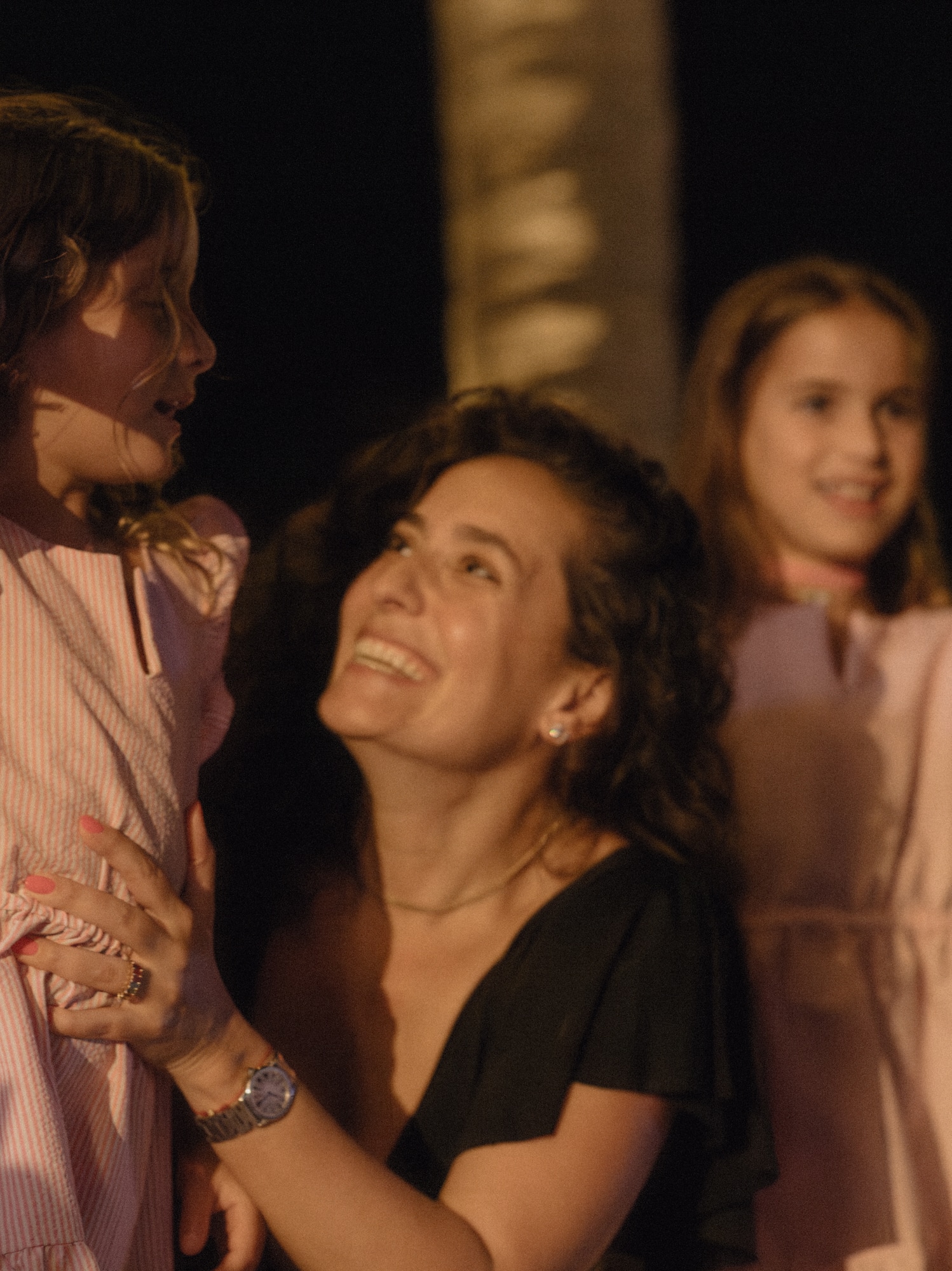 Happy woman with two girls, one holding a sword prop, at a night event.