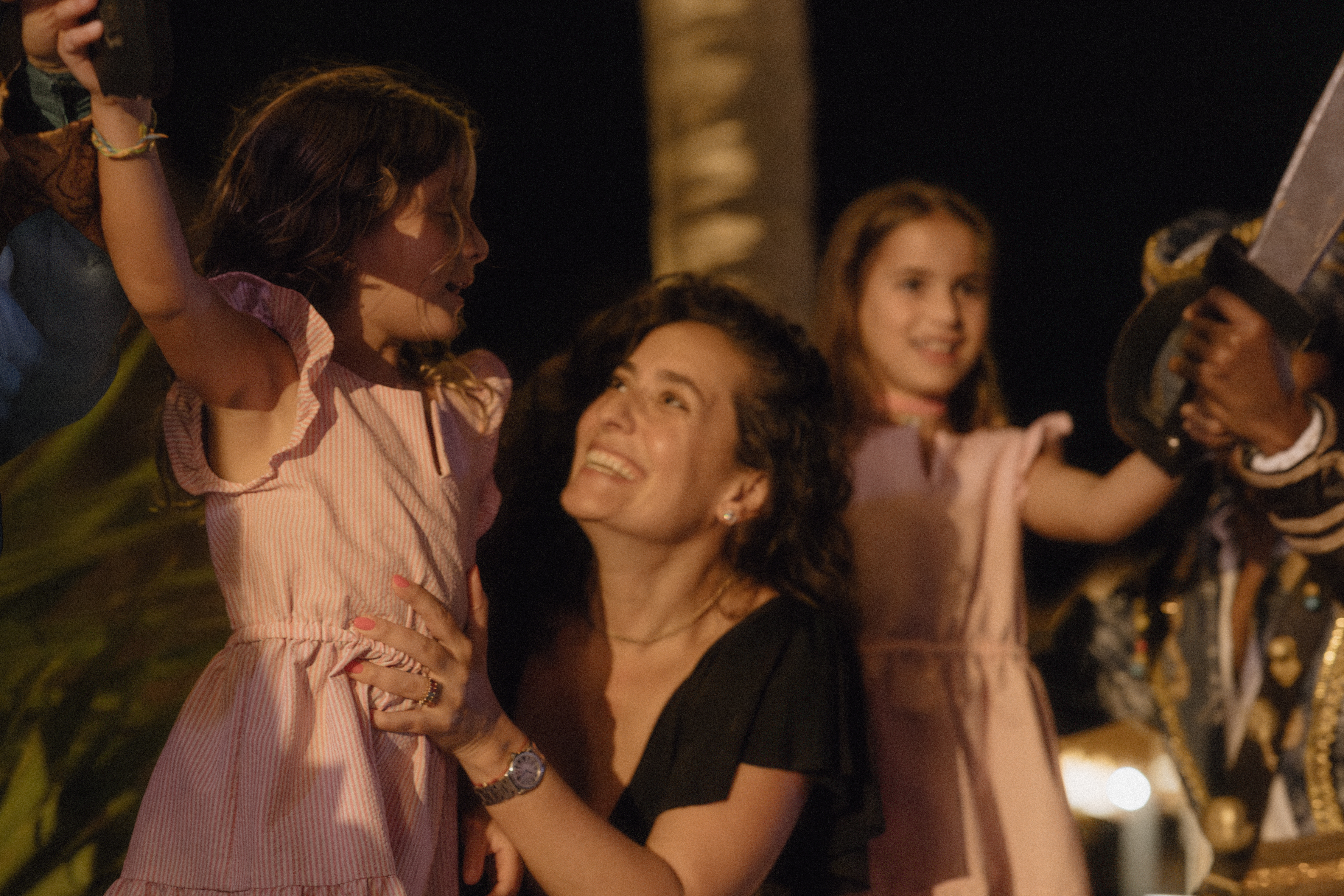 Happy woman with two girls, one holding a sword prop, at a night event.