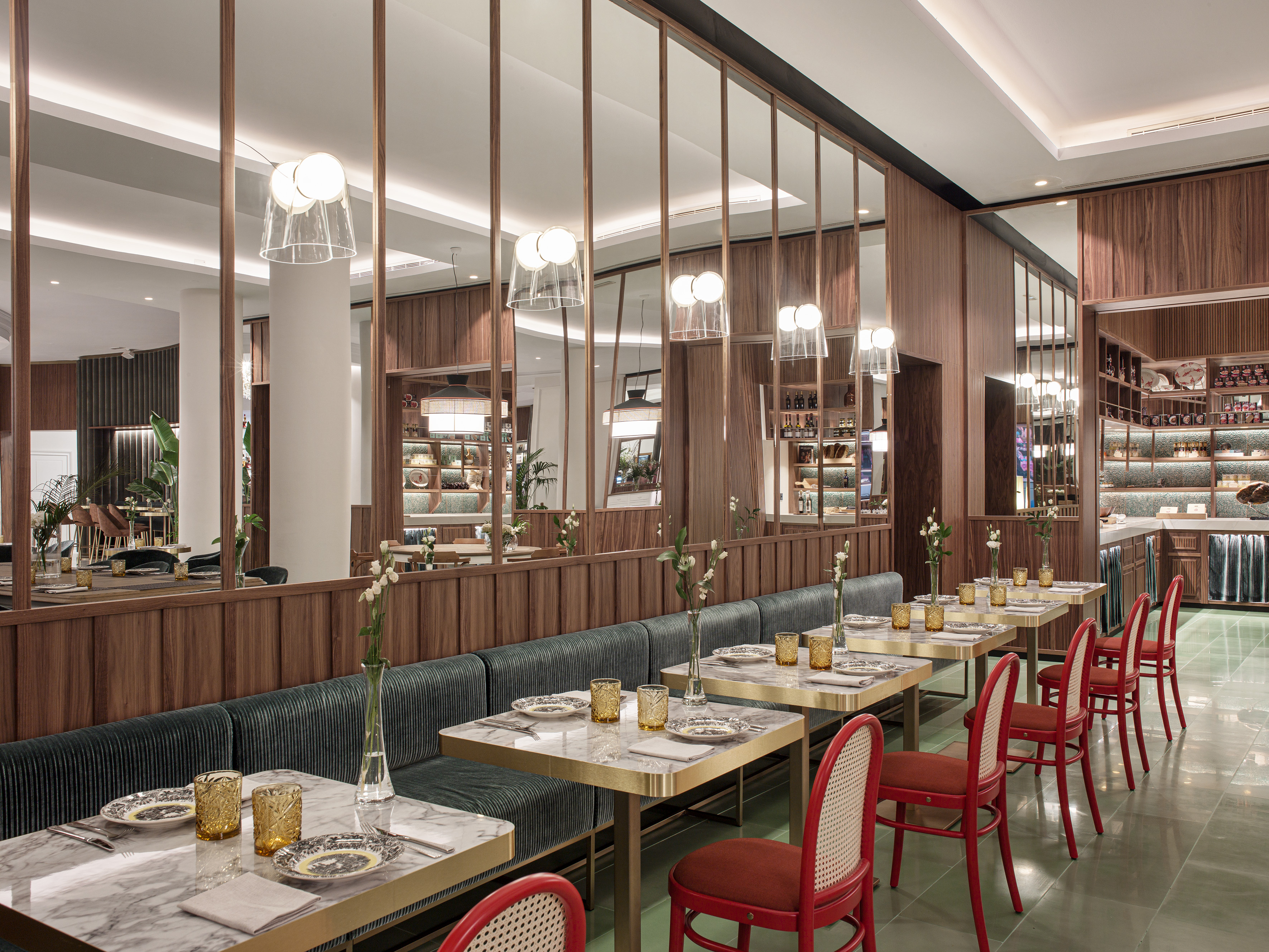 Modern restaurant dining room with marble tables, green banquettes, and red chairs.
