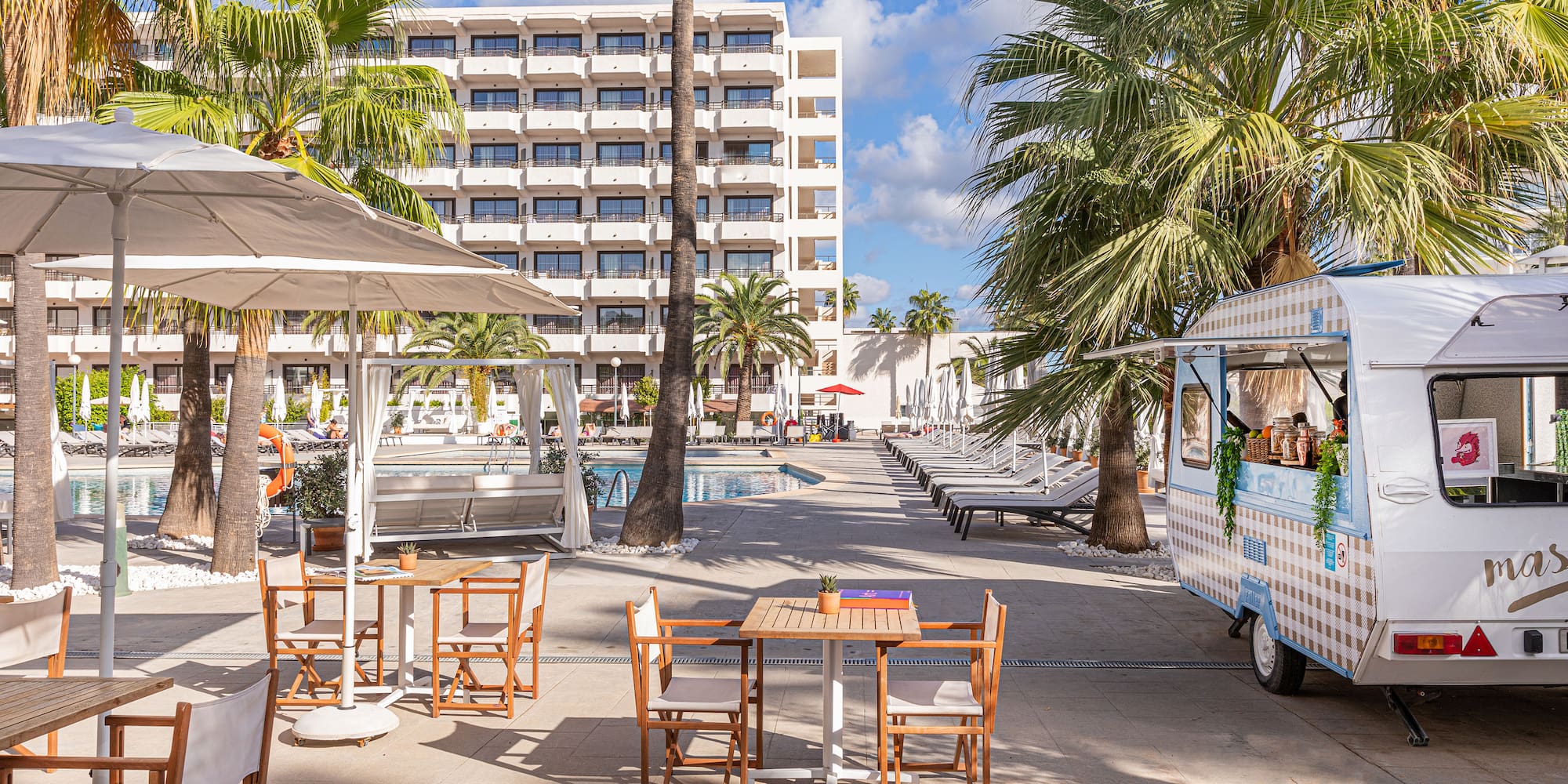 Hotel resort pool area with palm trees, outdoor dining, and a food truck.