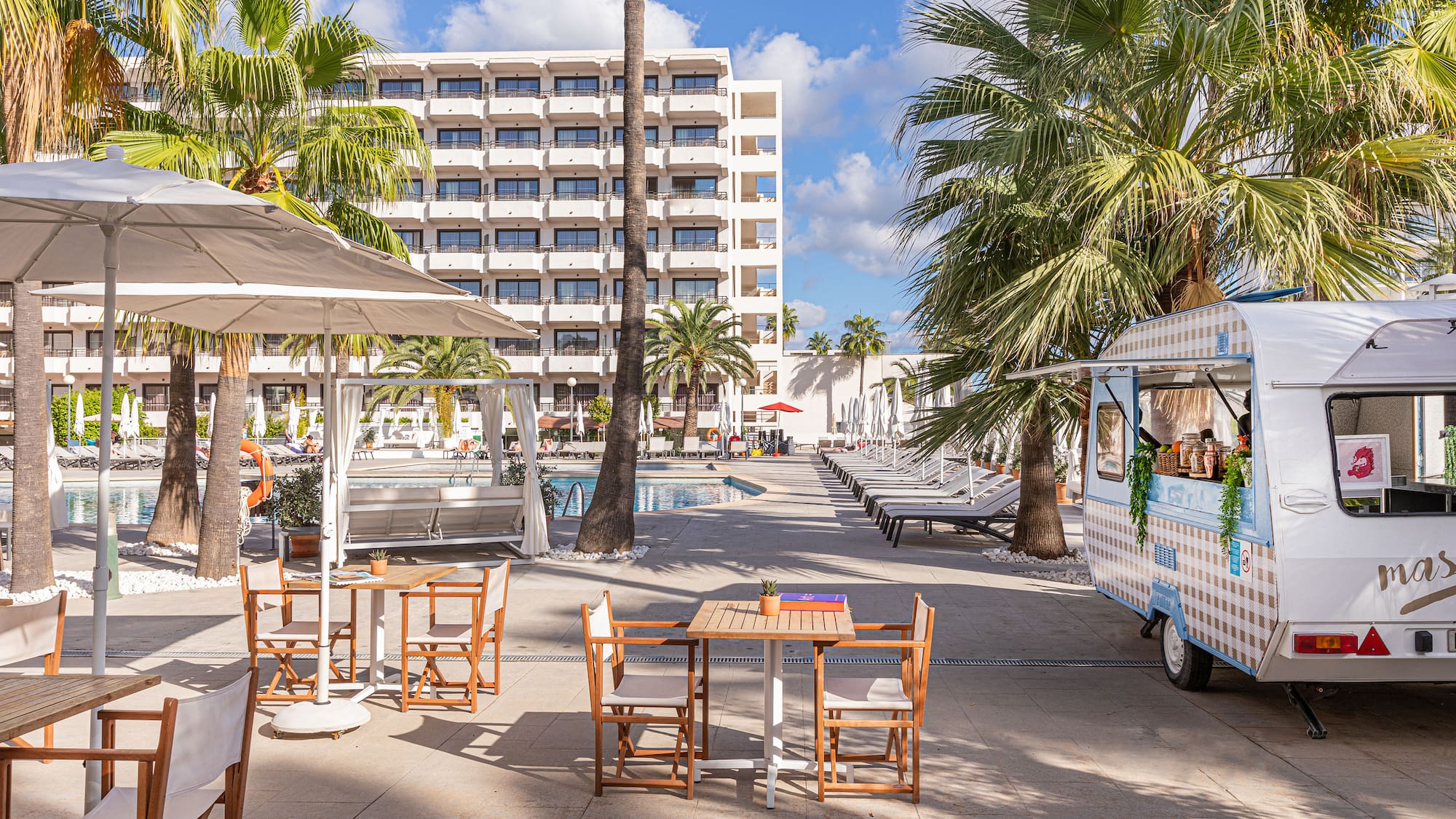 Hotel resort pool area with palm trees, outdoor dining, and a food truck.