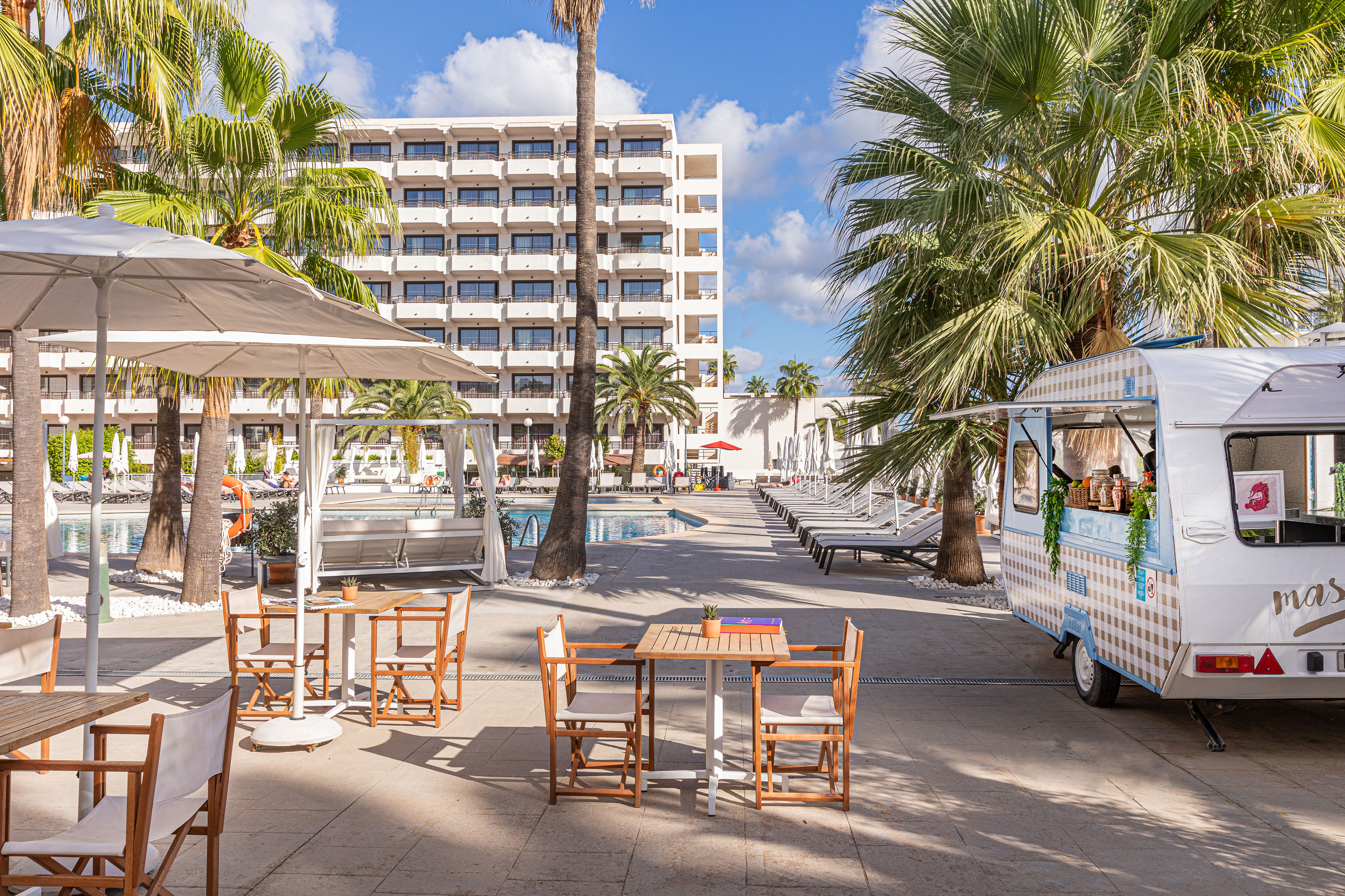 Hotel resort pool area with palm trees, outdoor dining, and a food truck.