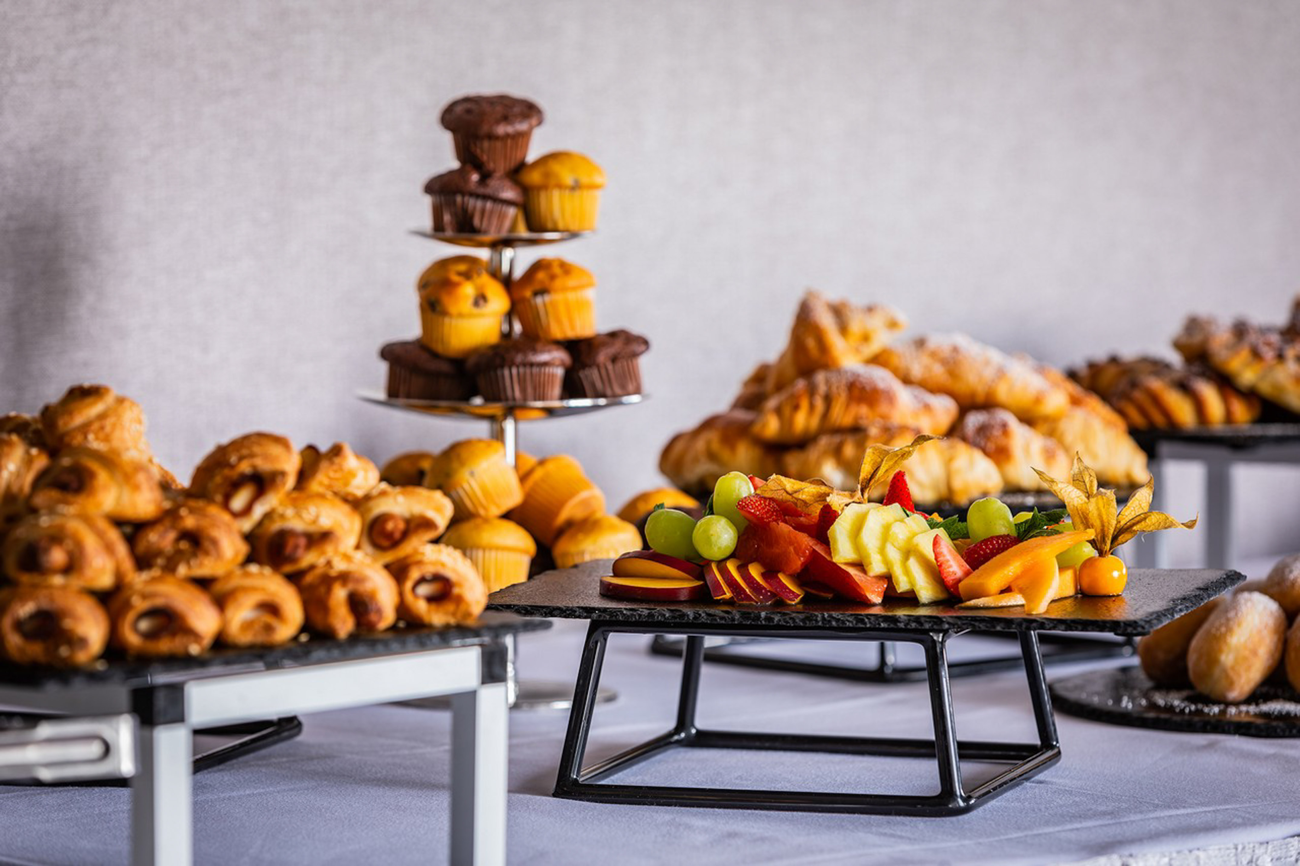 Catering buffet: muffins, croissants, pastries, and colorful fresh fruit platter.