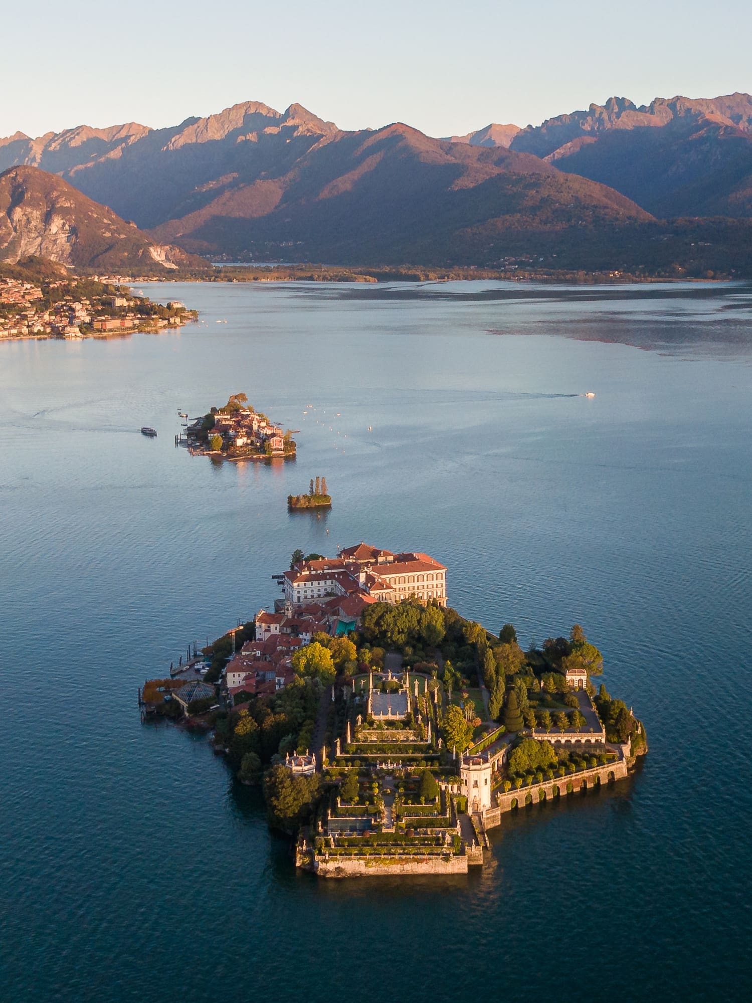 Aerial of Isola Bella, Lake Maggiore, with terraced gardens, palazzo, and mountains.