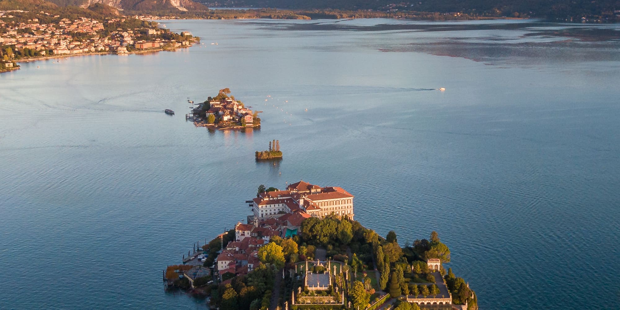 Aerial of Isola Bella, Lake Maggiore, with terraced gardens, palazzo, and mountains.