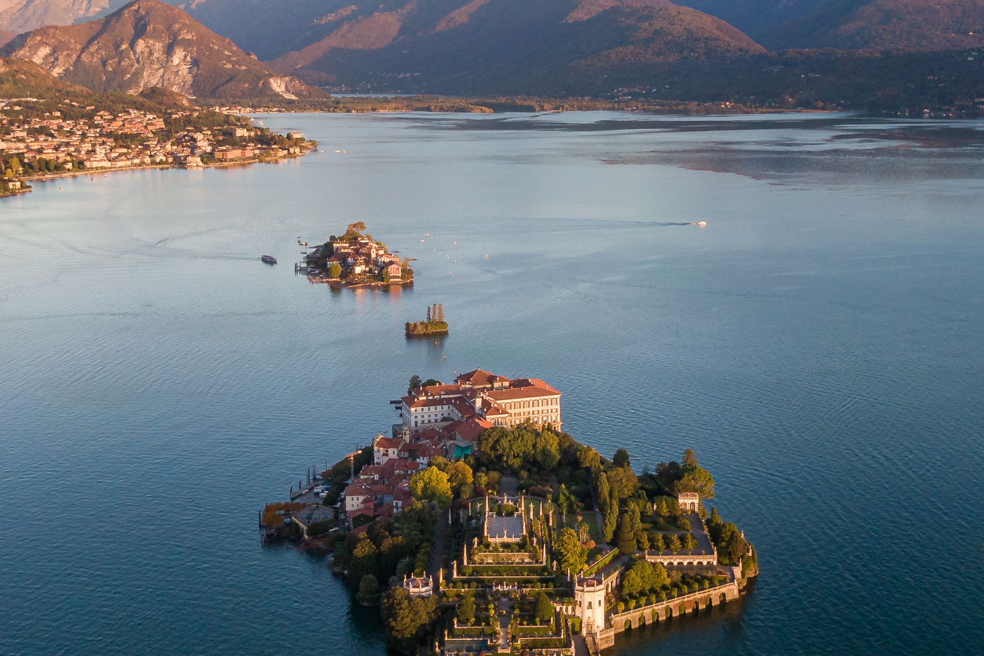 Aerial of Isola Bella, Lake Maggiore, with terraced gardens, palazzo, and mountains.