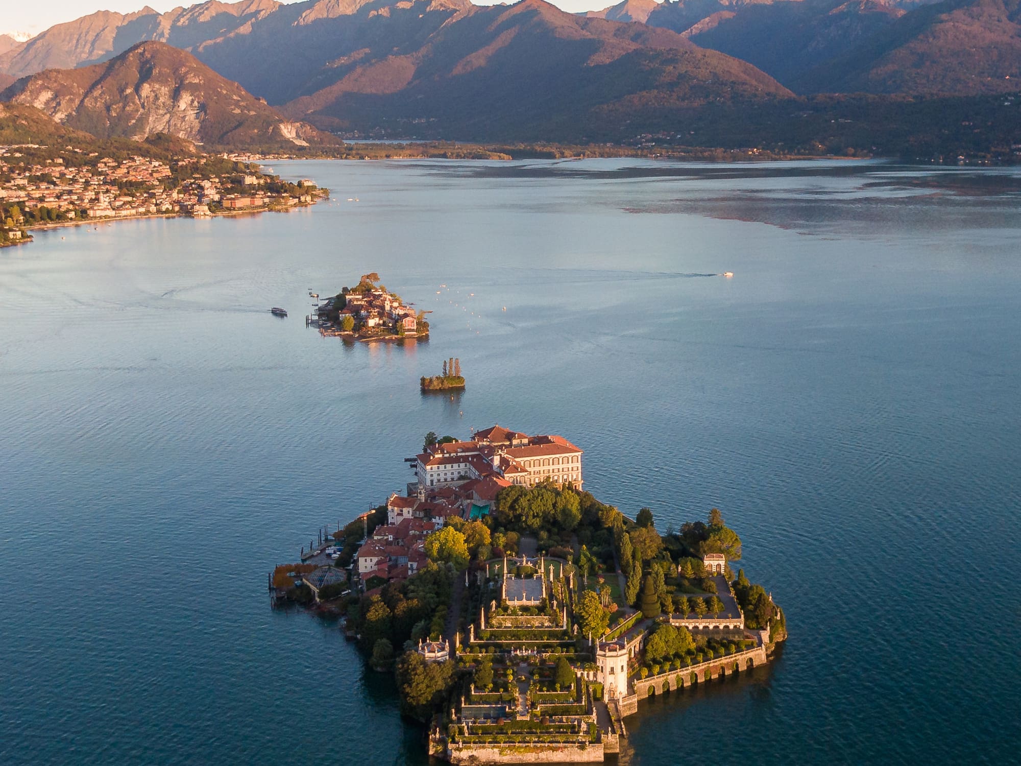 Aerial of Isola Bella, Lake Maggiore, with terraced gardens, palazzo, and mountains.