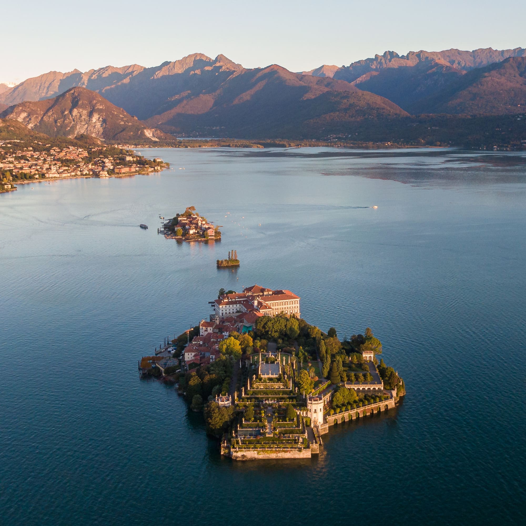 Aerial of Isola Bella, Lake Maggiore, with terraced gardens, palazzo, and mountains.