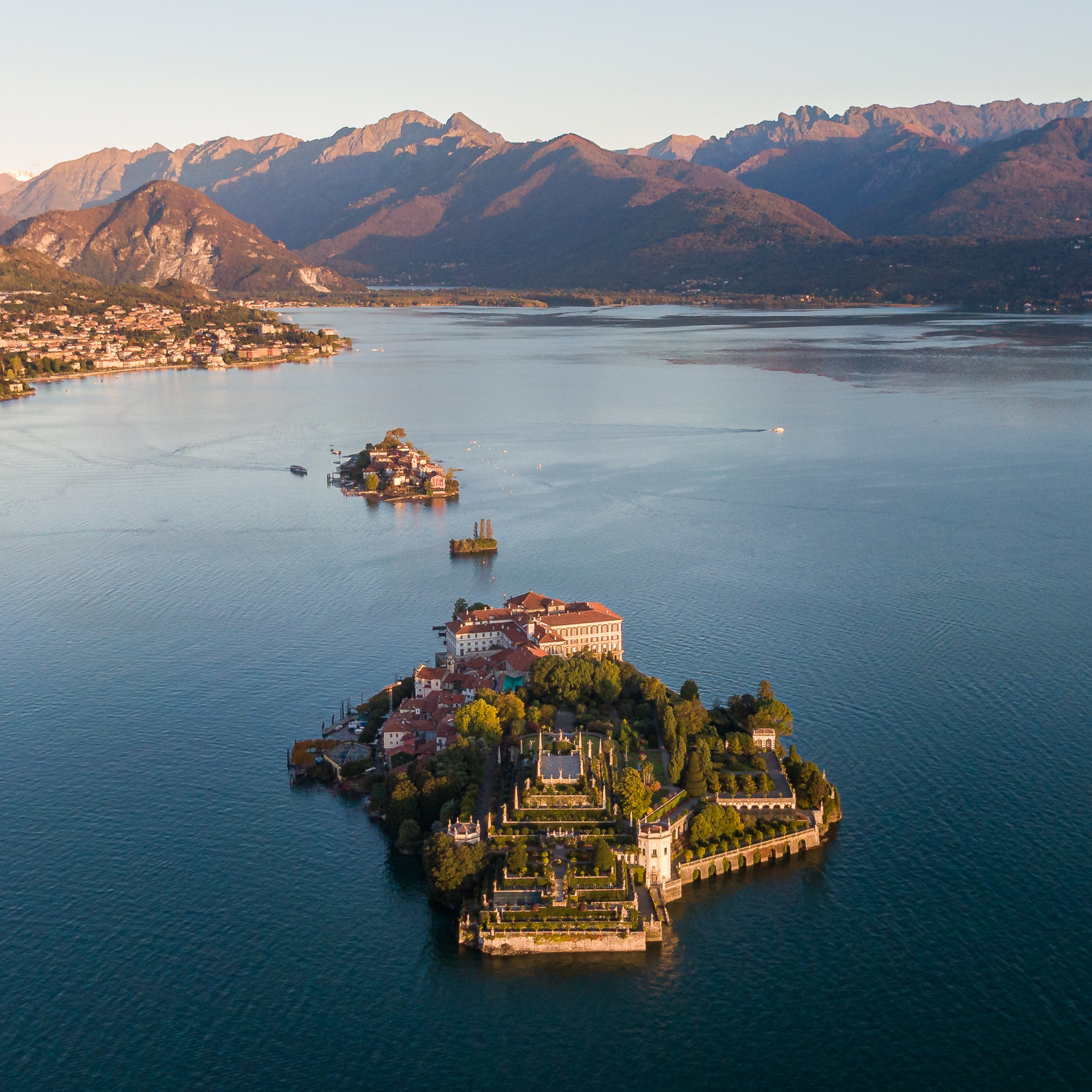 Aerial of Isola Bella, Lake Maggiore, with terraced gardens, palazzo, and mountains.