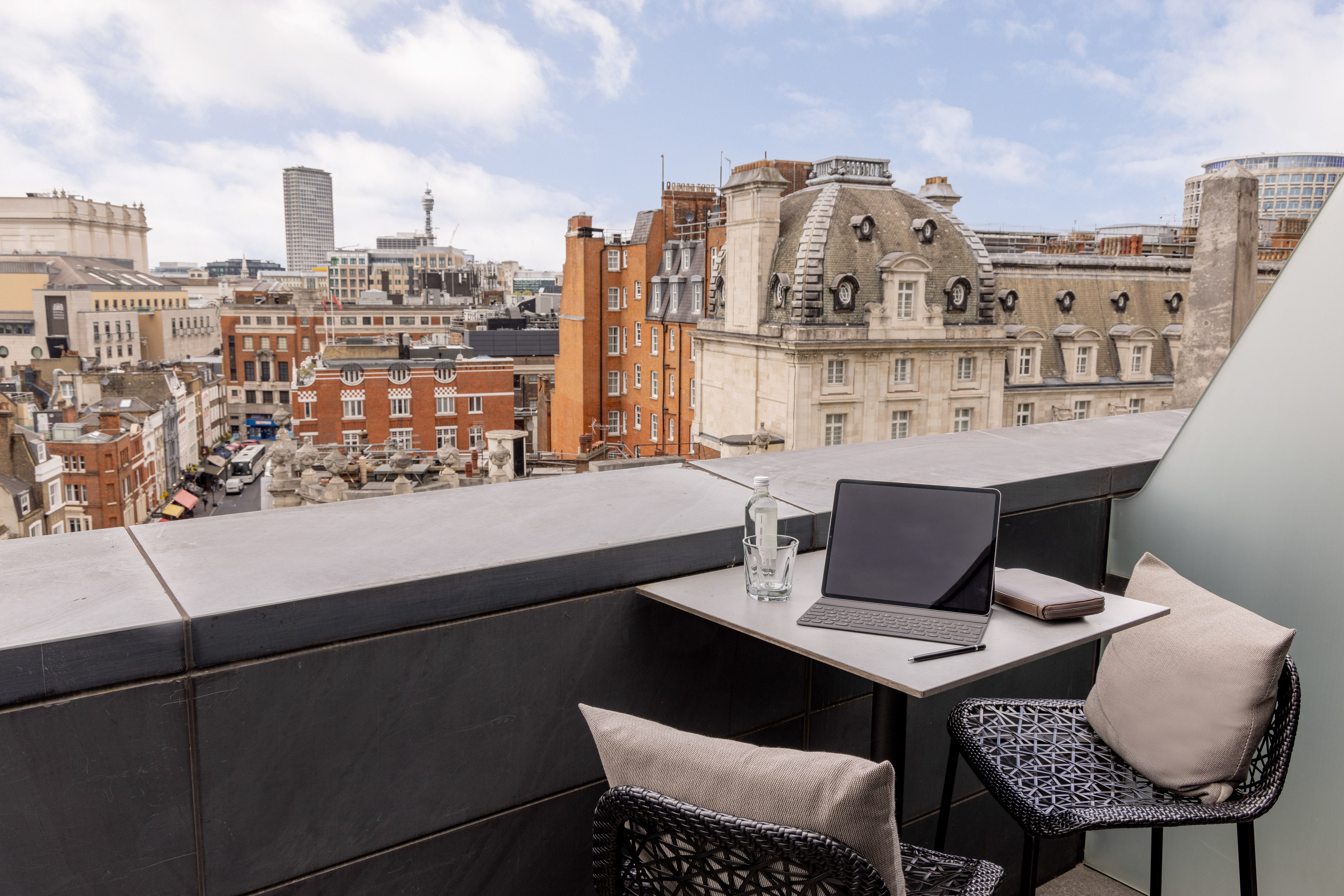 Balcony with laptop overlooking a bustling London cityscape and rooftops.